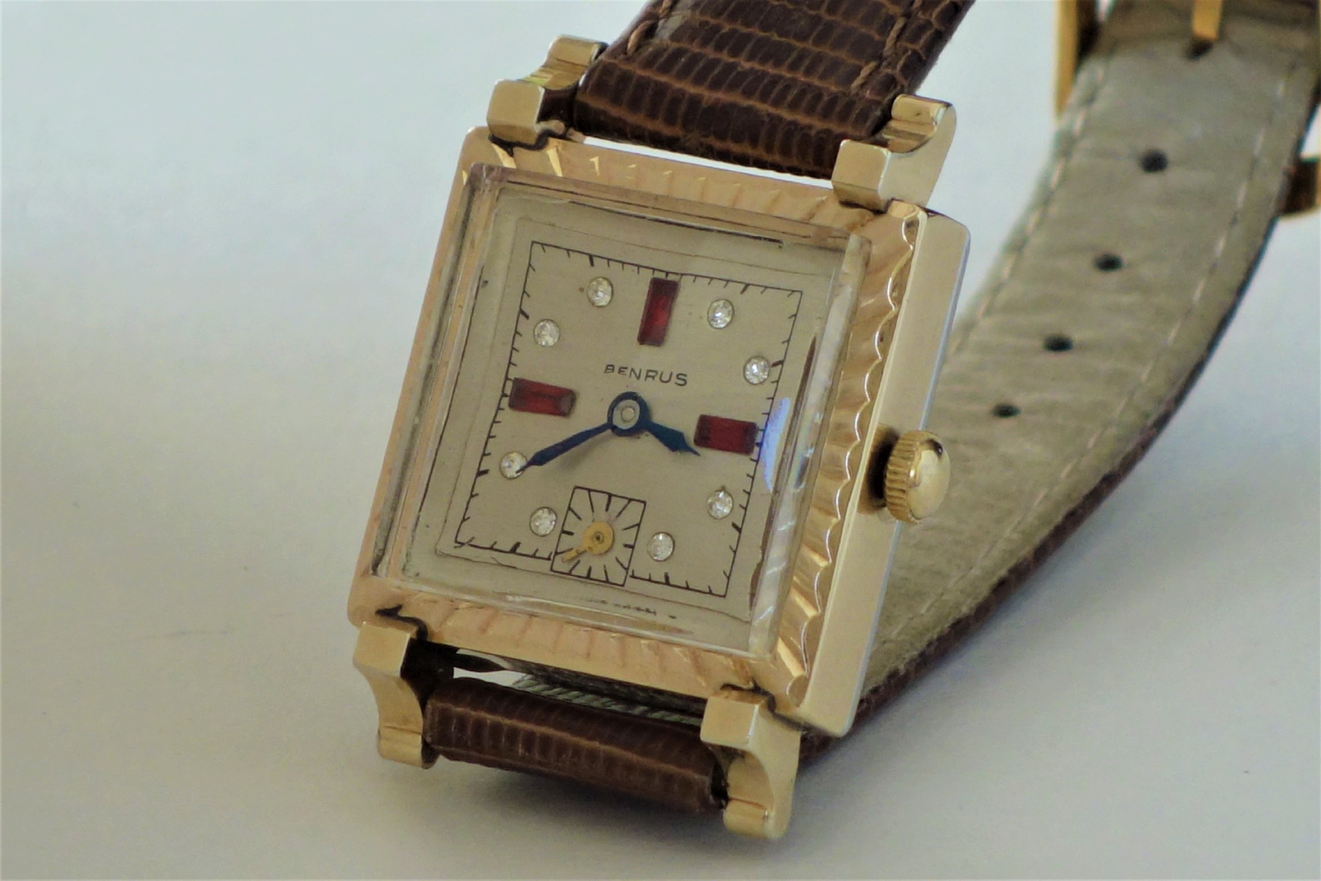 Eckige Armbanduhr von Benrus mit goldfarbenem Gehäuse, cremefarbenem Zifferblatt und braunem Lederarmband.