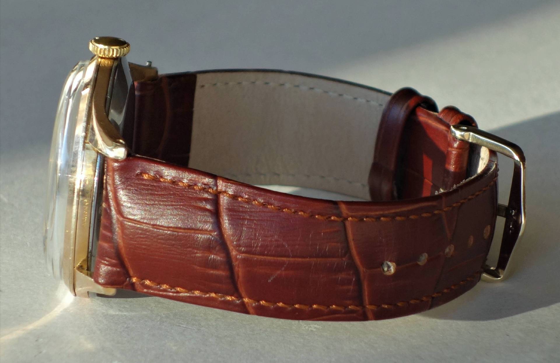 Armbanduhr mit braunem Armband und goldfarbenem Gehäuse.