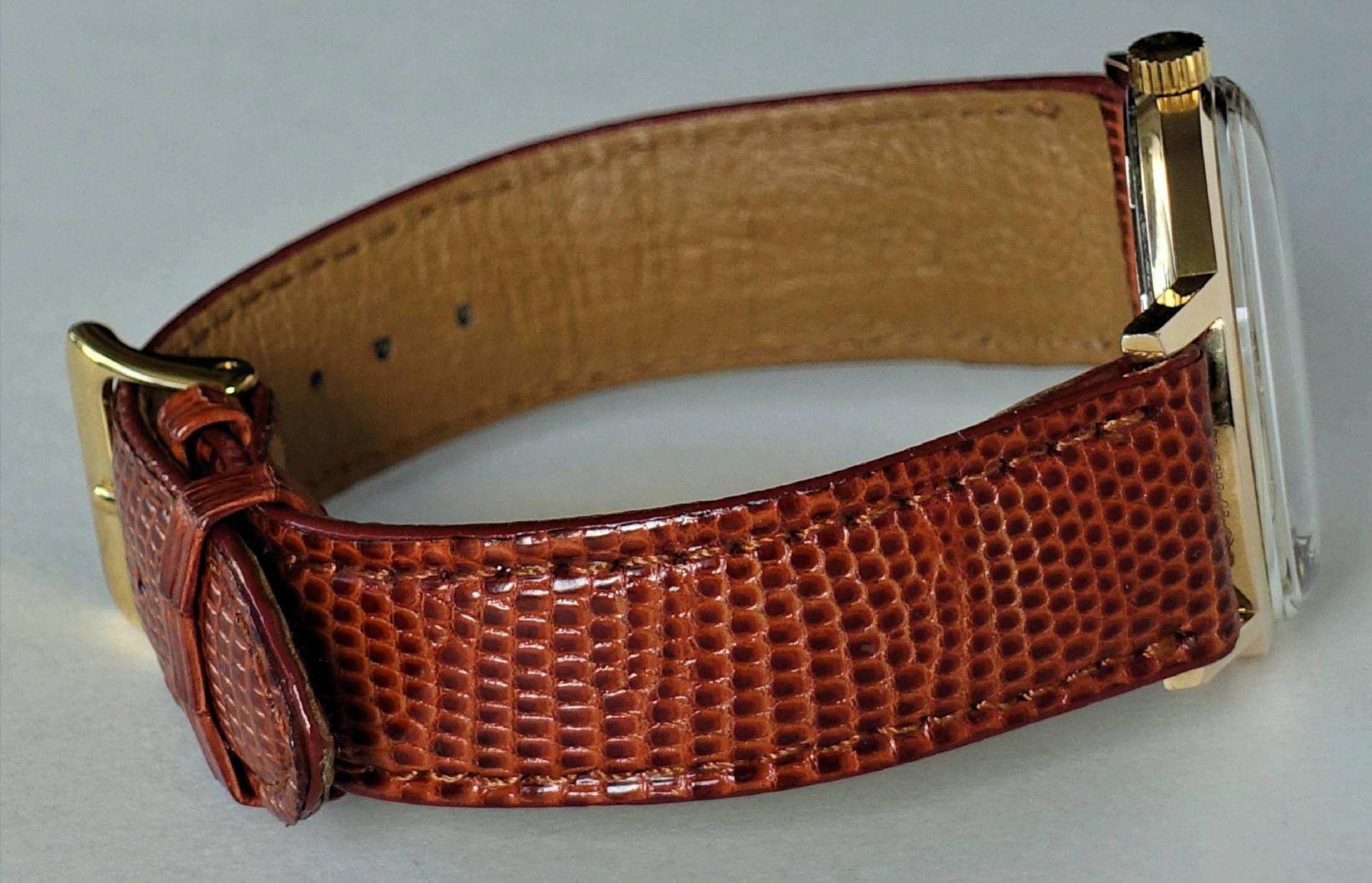 Braune Armbanduhr mit goldfarbenem Gehäuse und strukturierter Oberfläche am Lederarmband.