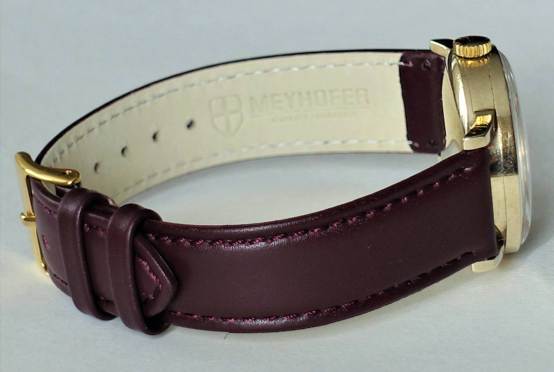 Detailaufnahme einer eleganten Armbanduhr mit braunem Lederarmband und goldenen Akzenten.
