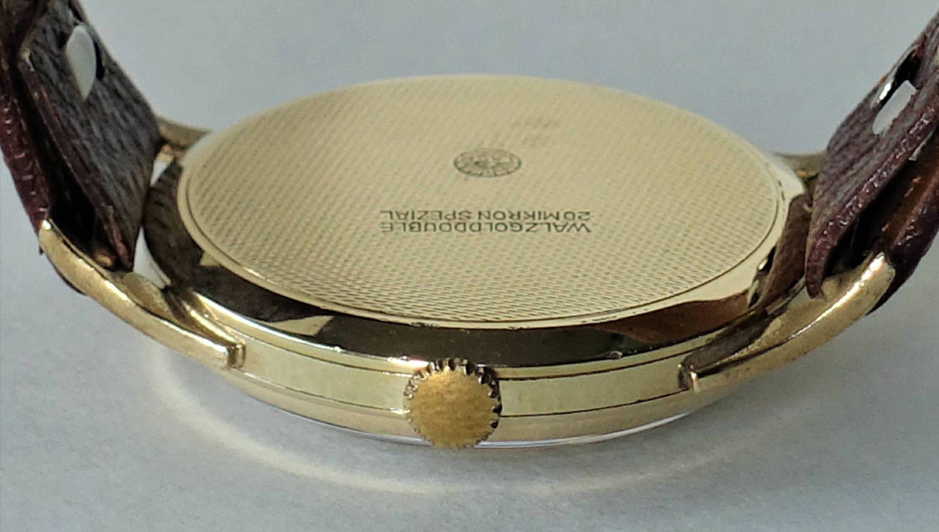 Rückseite einer Armbanduhr mit goldfarbenem Gehäuse und braunem Lederarmband.