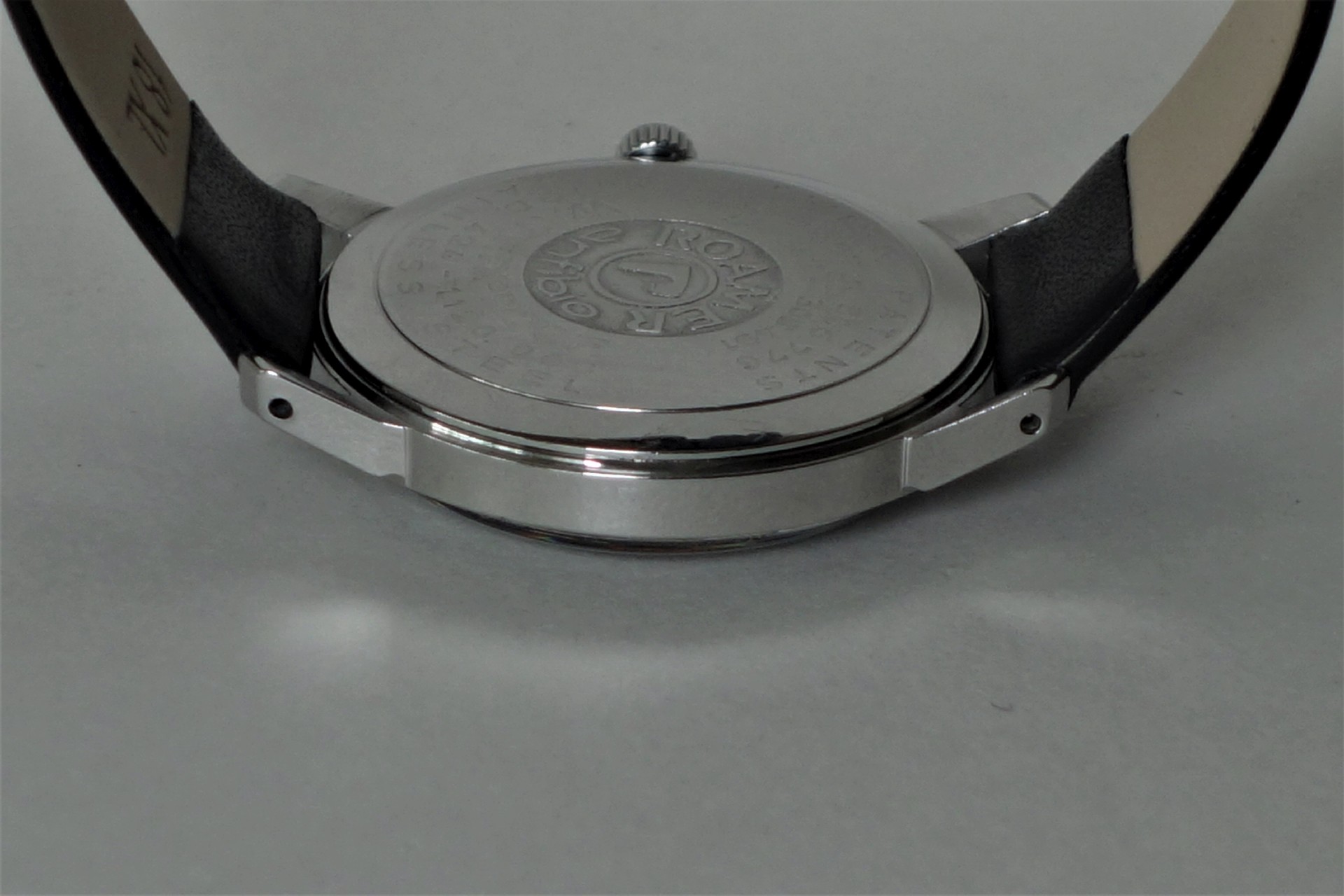 Runder silberfarbener Uhrenboden mit Gravur an einer Armbanduhr.