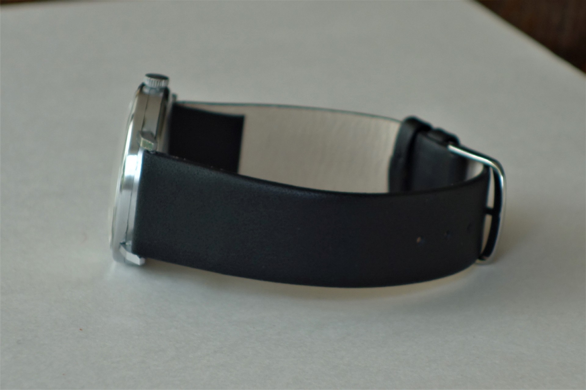 Schwarzes Armband an einer Armbanduhr mit silberfarbenem Gehäuse.