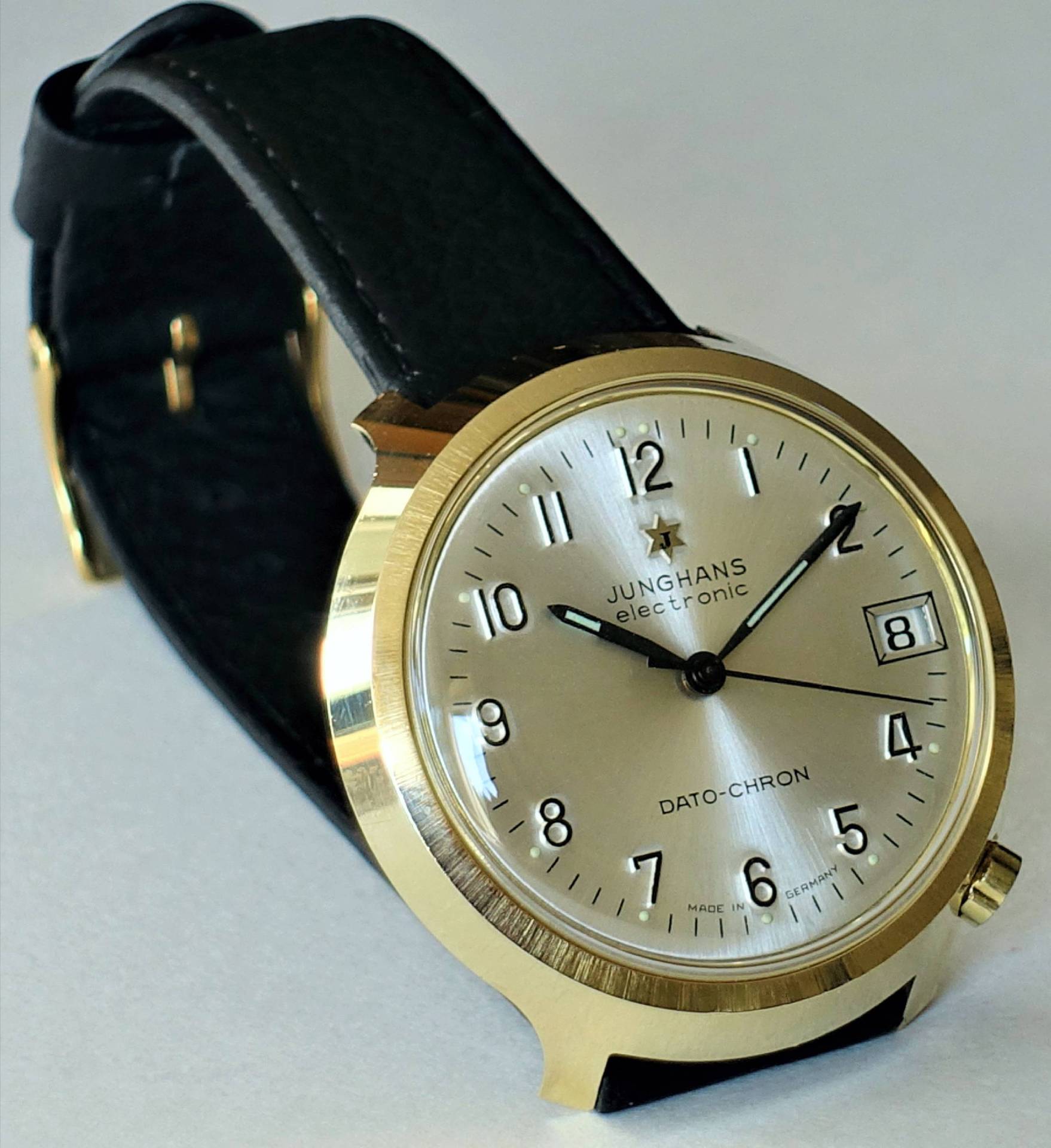 Analoge Armbanduhr mit goldfarbenem Gehäuse, silberfarbenem Zifferblatt und schwarzem Armband.