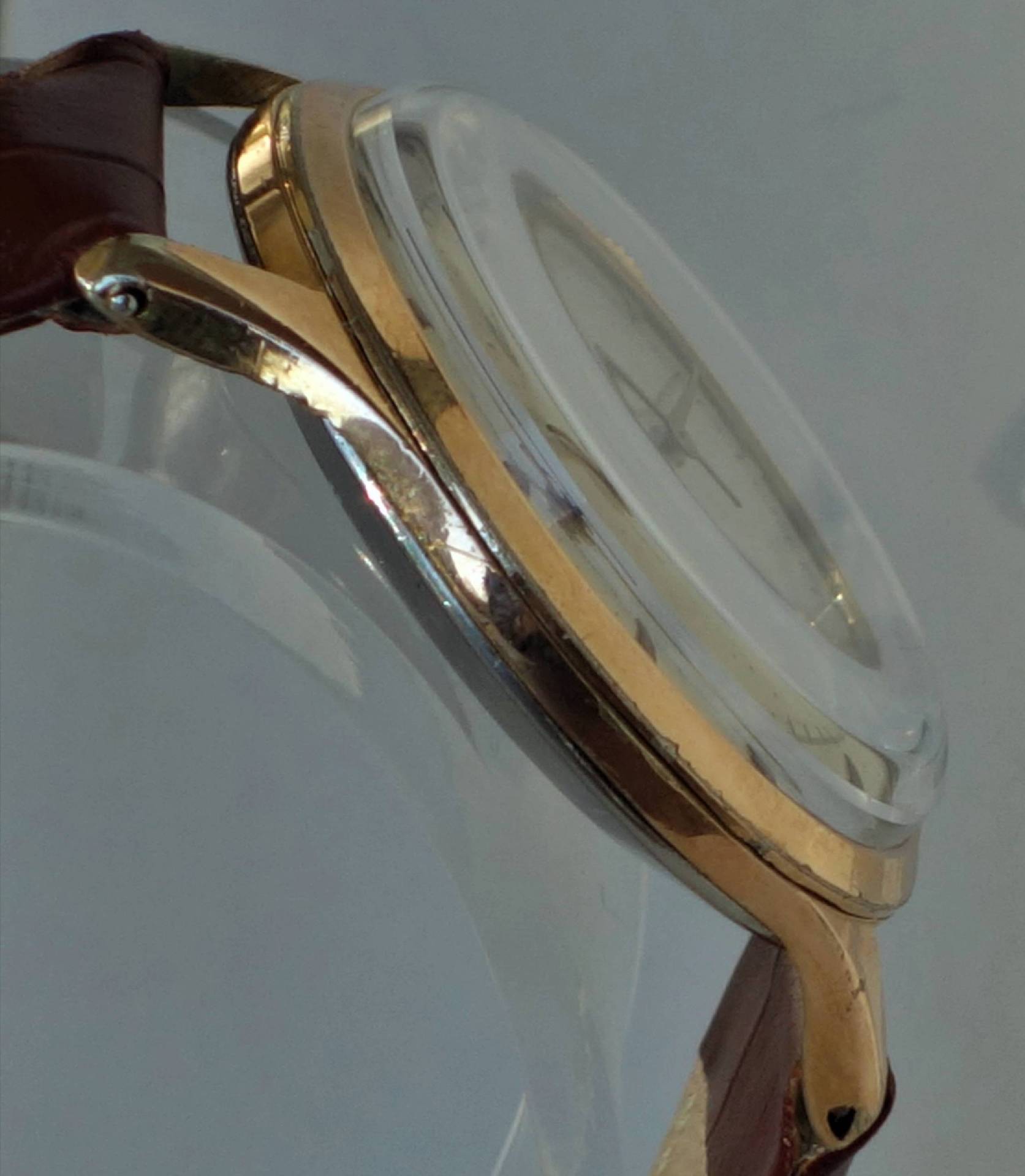 Goldfarbenes Uhrgehäuse mit braunem Armband und gewölbtem Glas.