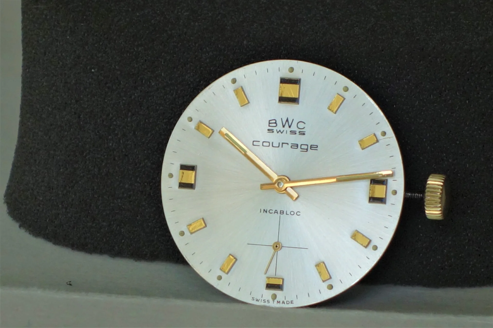 Uhrwerk BWC Swiss Courage Rundes Uhrwerk mit silberfarbenem Zifferblatt, goldfarbenen Zeigern und Indizes, sowie seitlicher Krone.
