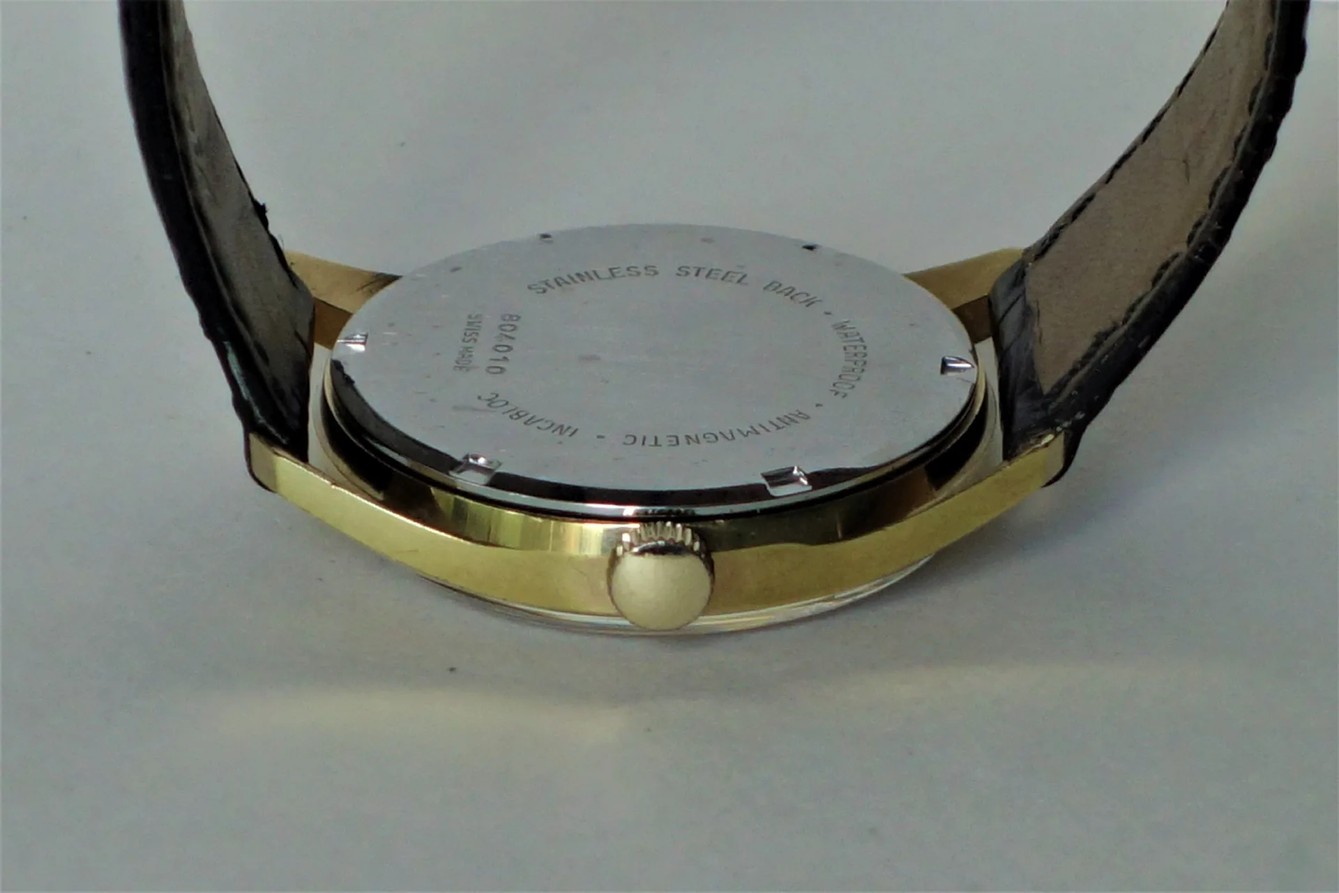 Runder Edelstahlboden einer Armbanduhr mit Gravur und goldfarbenem Gehäuse.