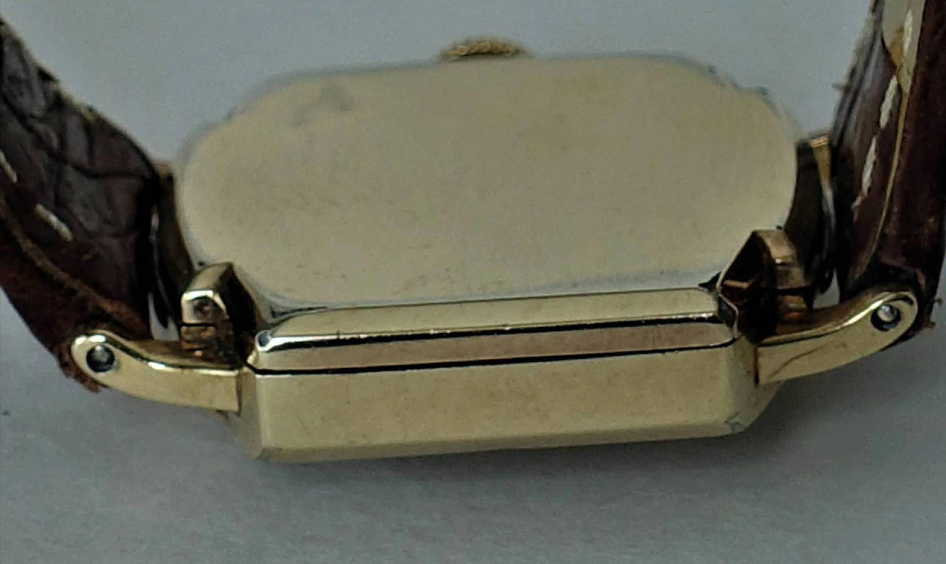Nahaufnahme eines rechteckigen, gelbfarbenen Uhrgehäuses mit braunem Lederarmband und sichtbaren Scharnieren.