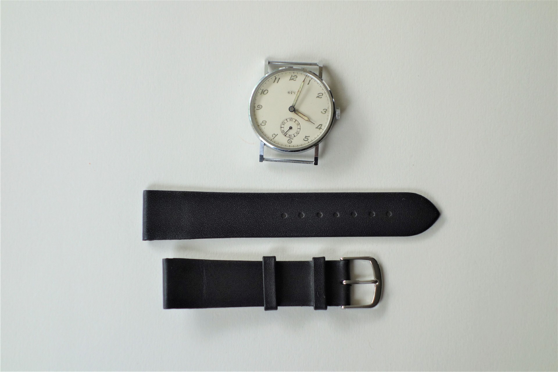 Zerlegte Armbanduhr mit hellem Zifferblatt und schwarzem Armband aus zwei Teilen.