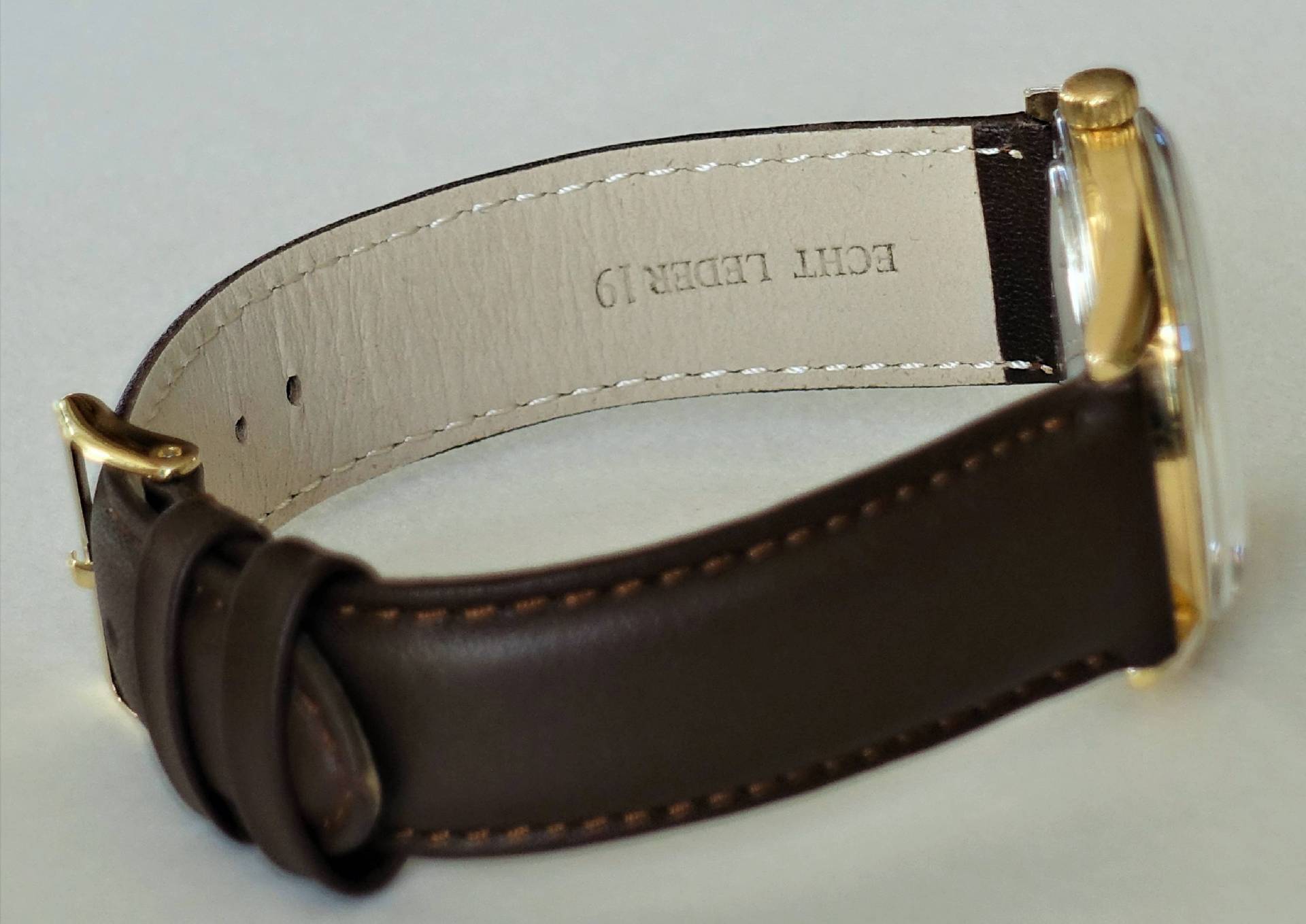 Braune Armbanduhr mit goldfarbenem Gehäuse und Dornschließe.