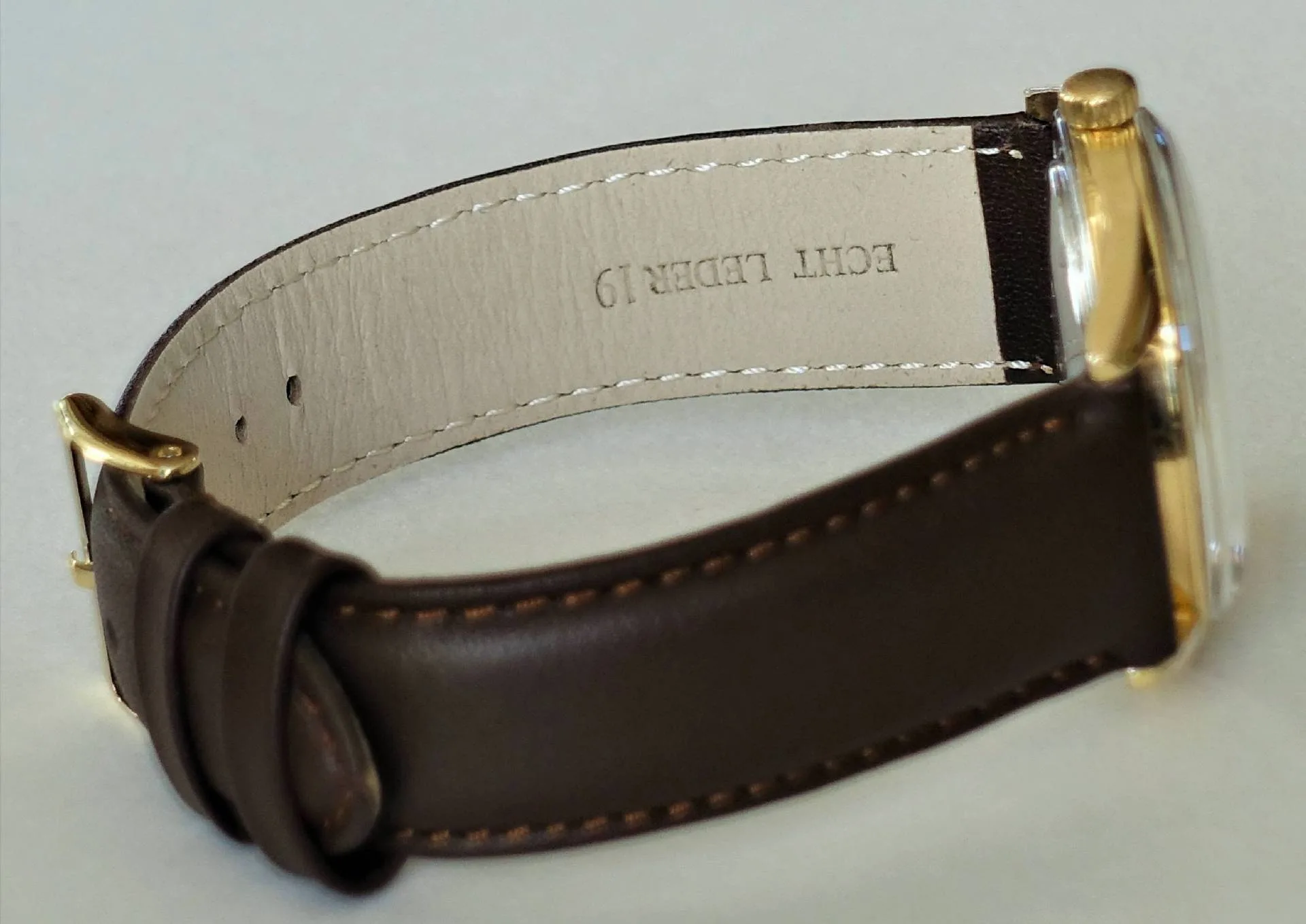 Braune Armbanduhr mit goldfarbenem Gehäuse und Dornschließe.