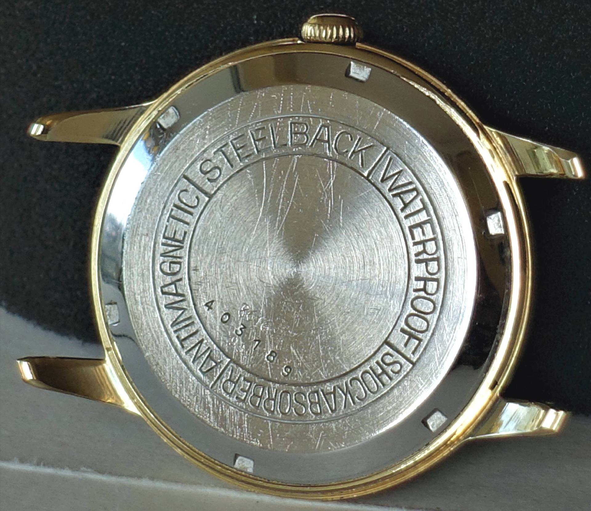 Silberfarbener Uhrenboden mit Gravur und goldfarbenem Gehäuserand.