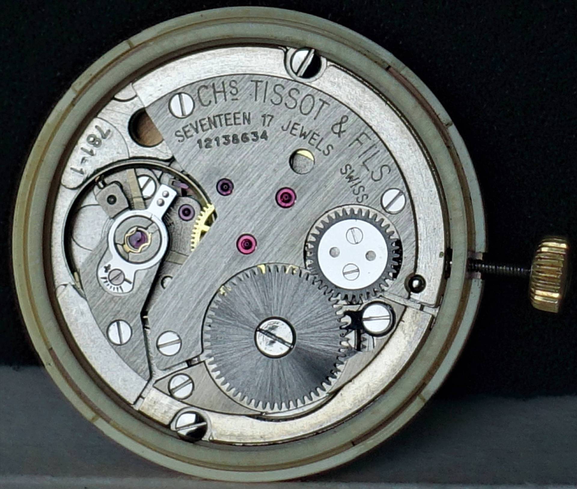 Silberfarbenes mechanisches Uhrwerk mit sichtbaren Zahnrädern und goldfarbener Krone.
