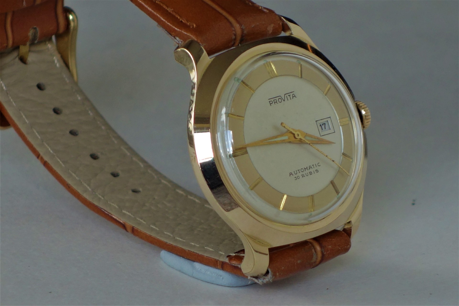 Runde Armbanduhr mit hellem Zifferblatt, goldfarbenem Gehäuse und braunem Lederarmband.