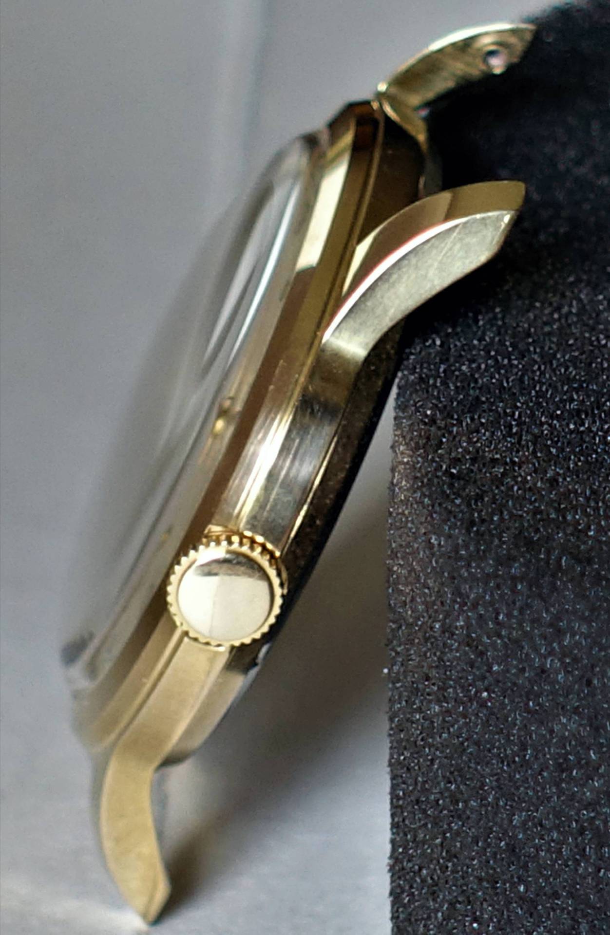 Seitliches Uhrengehäuse in goldfarbener Ausführung mit Krone.