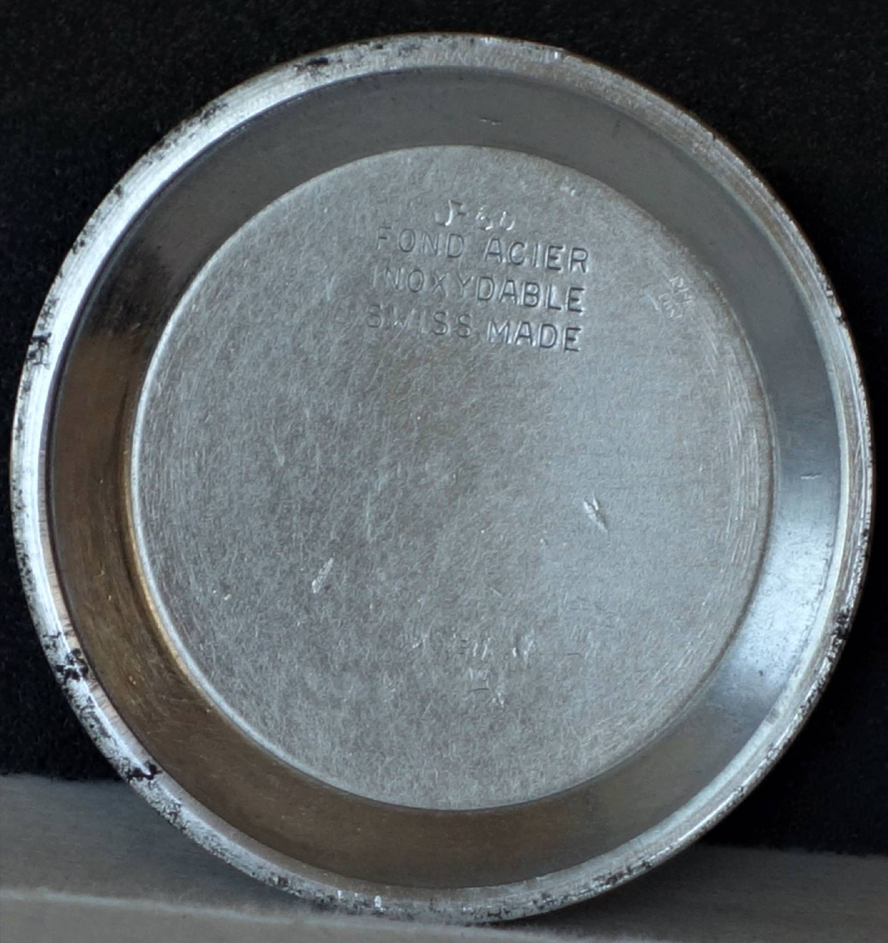 Runder silberfarbener Gehäuseboden für Armbanduhren mit eingeprägter Beschriftung.