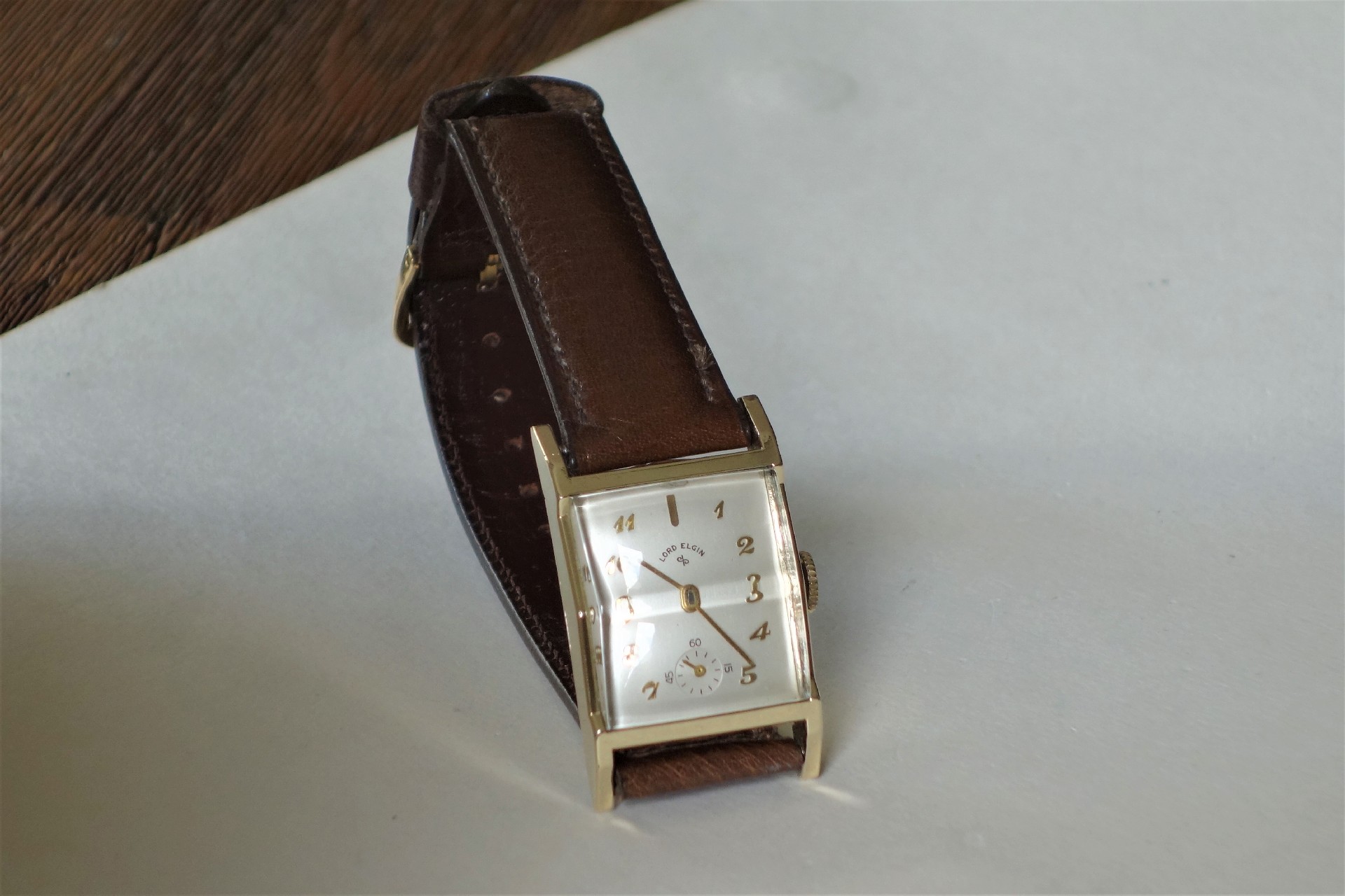 Rechteckige Armbanduhr mit braunem Armband und hellem Zifferblatt.