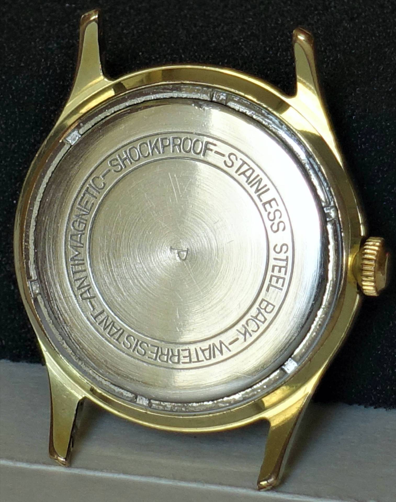 Rundes Uhrgehäuse in goldfarbener Ausführung mit silberfarbener Rückseite.