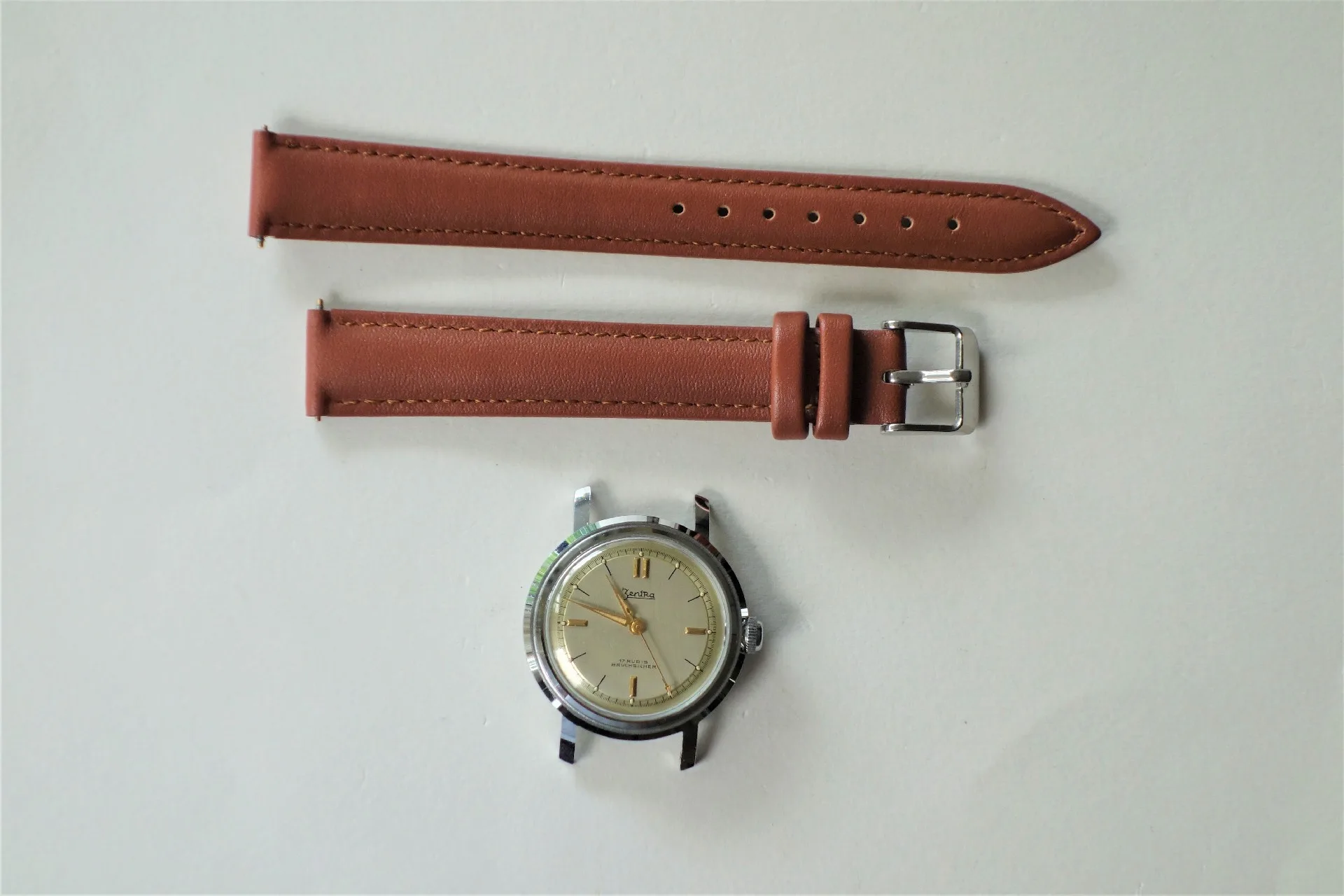 Uhrgehäuse silberfarben und Armband braun Silberfarbenes Uhrgehäuse mit hellem Zifferblatt und braunes Armband in zwei Teilen.