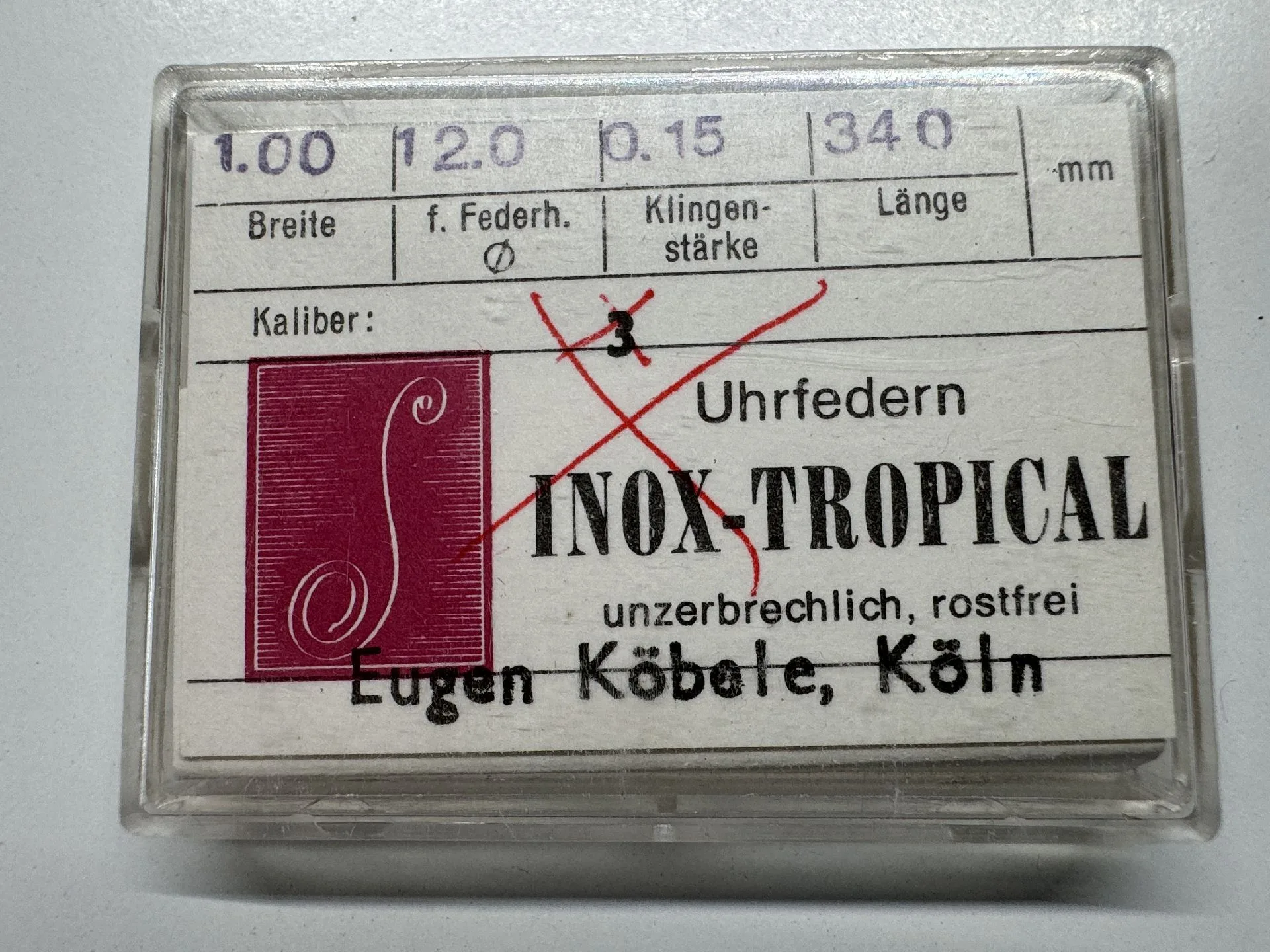 Ersatz-Uhrfeder in transparenter Kunststoffbox mit Beschriftung für Uhrenreparatur.