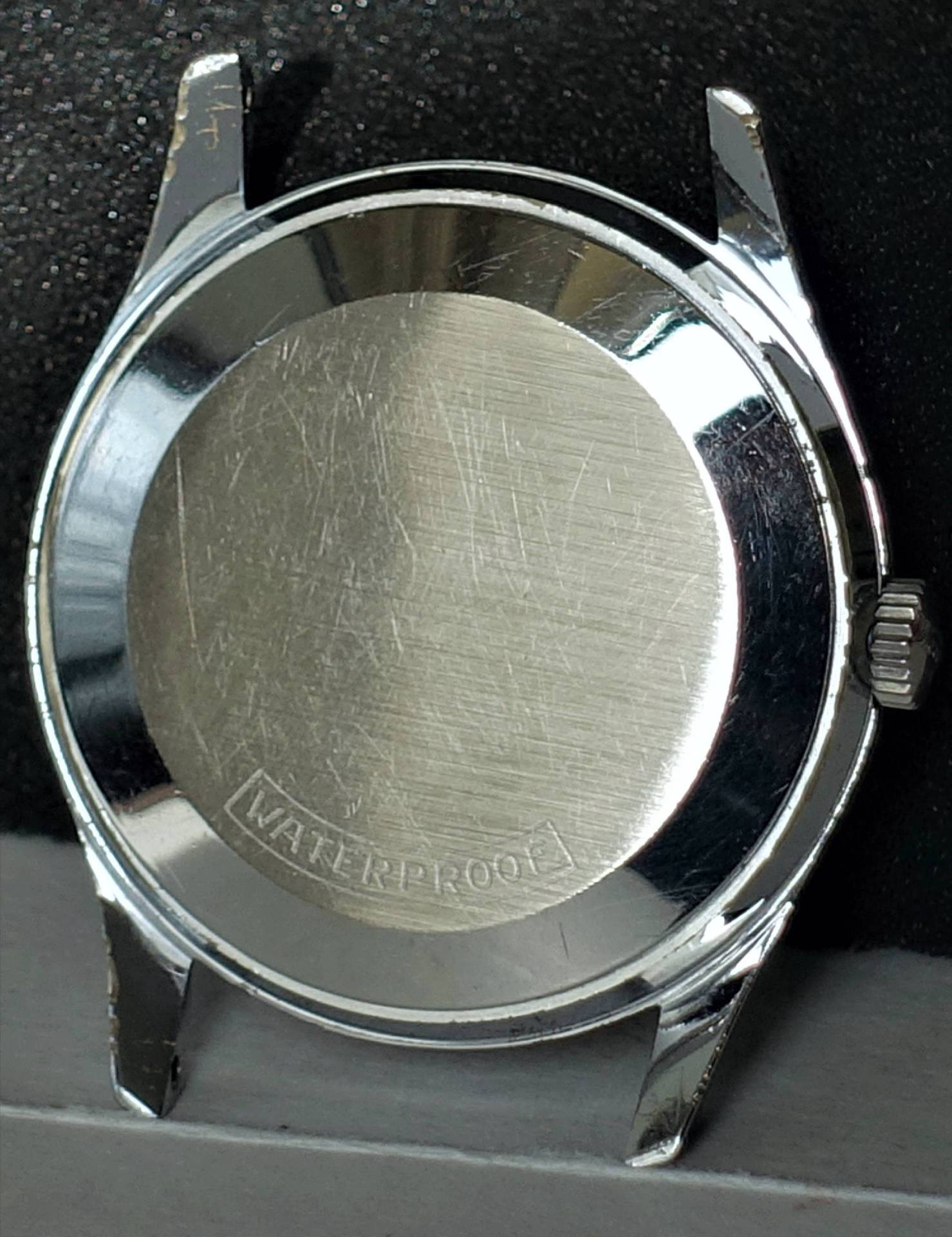 Silberfarbenes Uhrengehäuse mit verschraubtem Boden und seitlicher Krone.