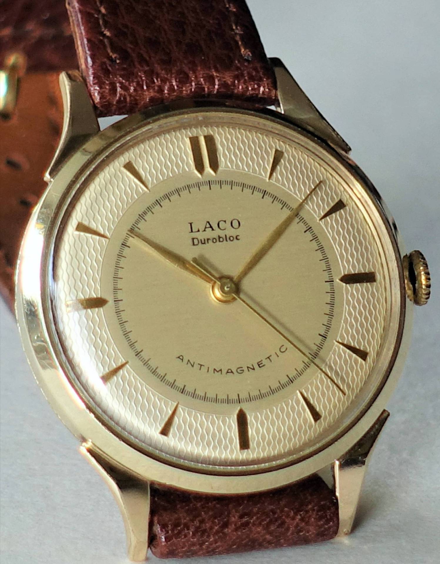 Goldfarbene Armbanduhr mit braunem Lederarmband und strukturierter Zifferblattmitte.