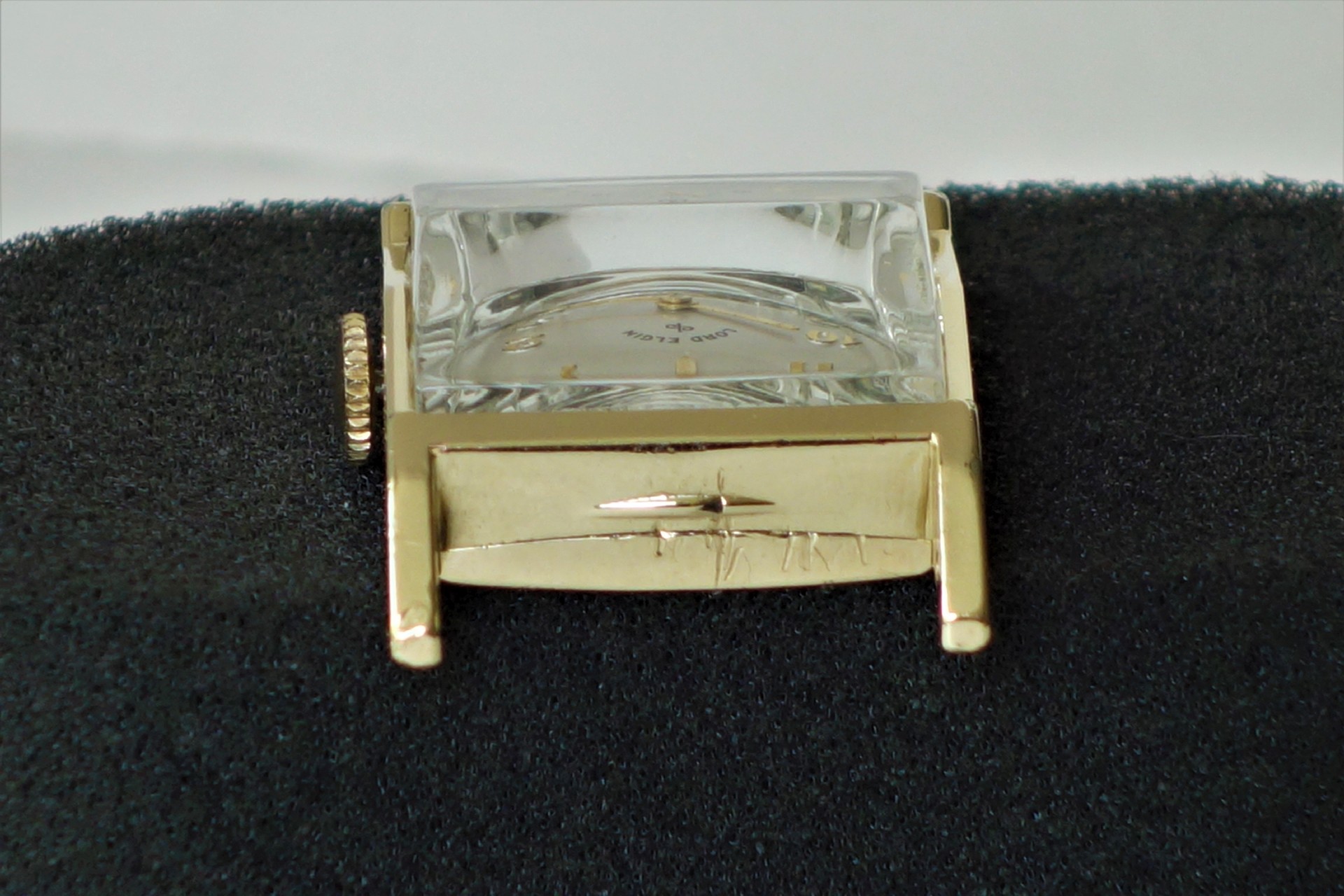 Eckiges Uhrengehäuse in goldfarbener Optik mit aufgesetztem Glas und sichtbarer Krone.