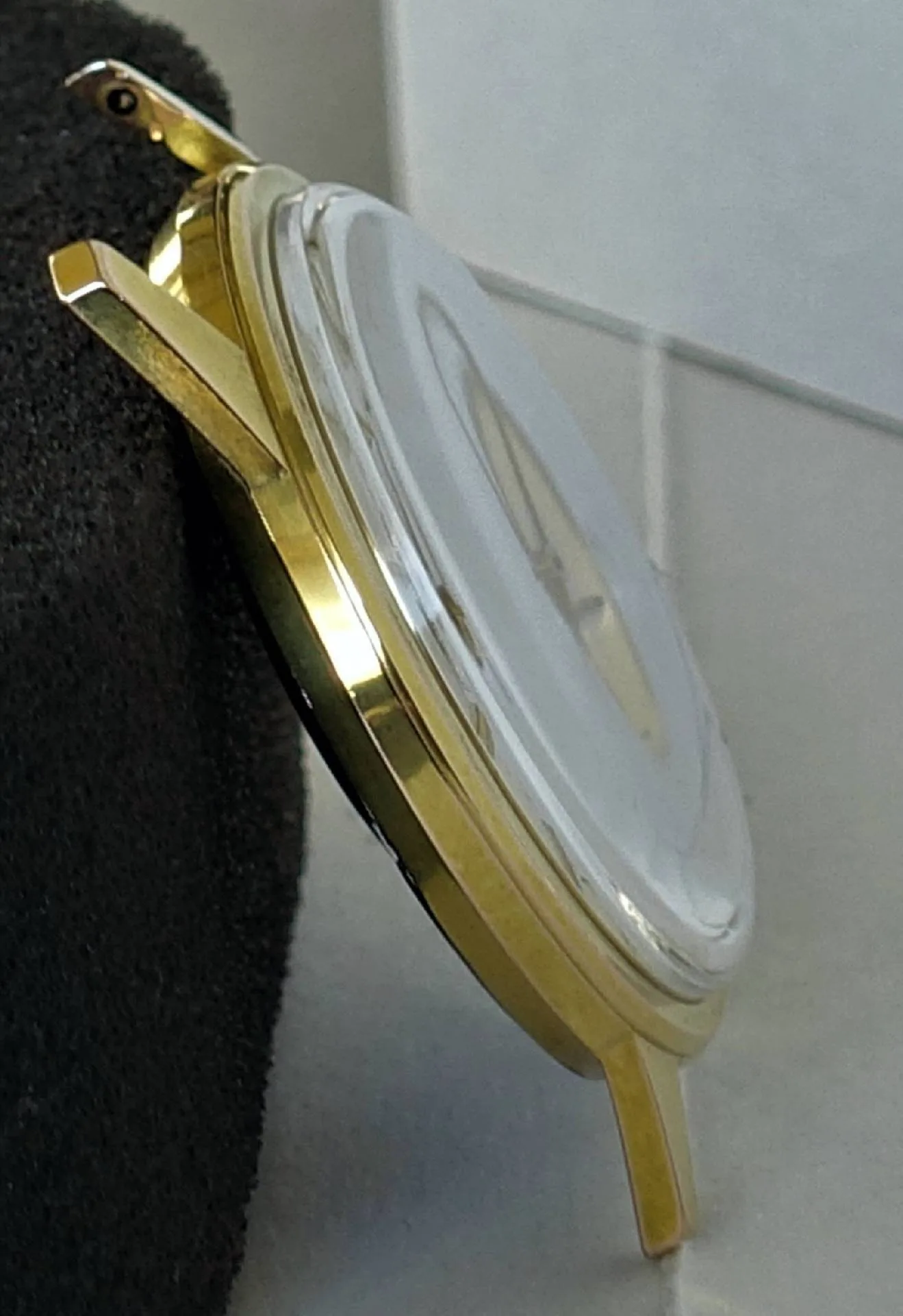 Das Bild zeigt das seitliche Profil eines flachen Uhrgehäuses in glänzendem Gelb mit stark gewölbtem, transparentem Uhrglas.