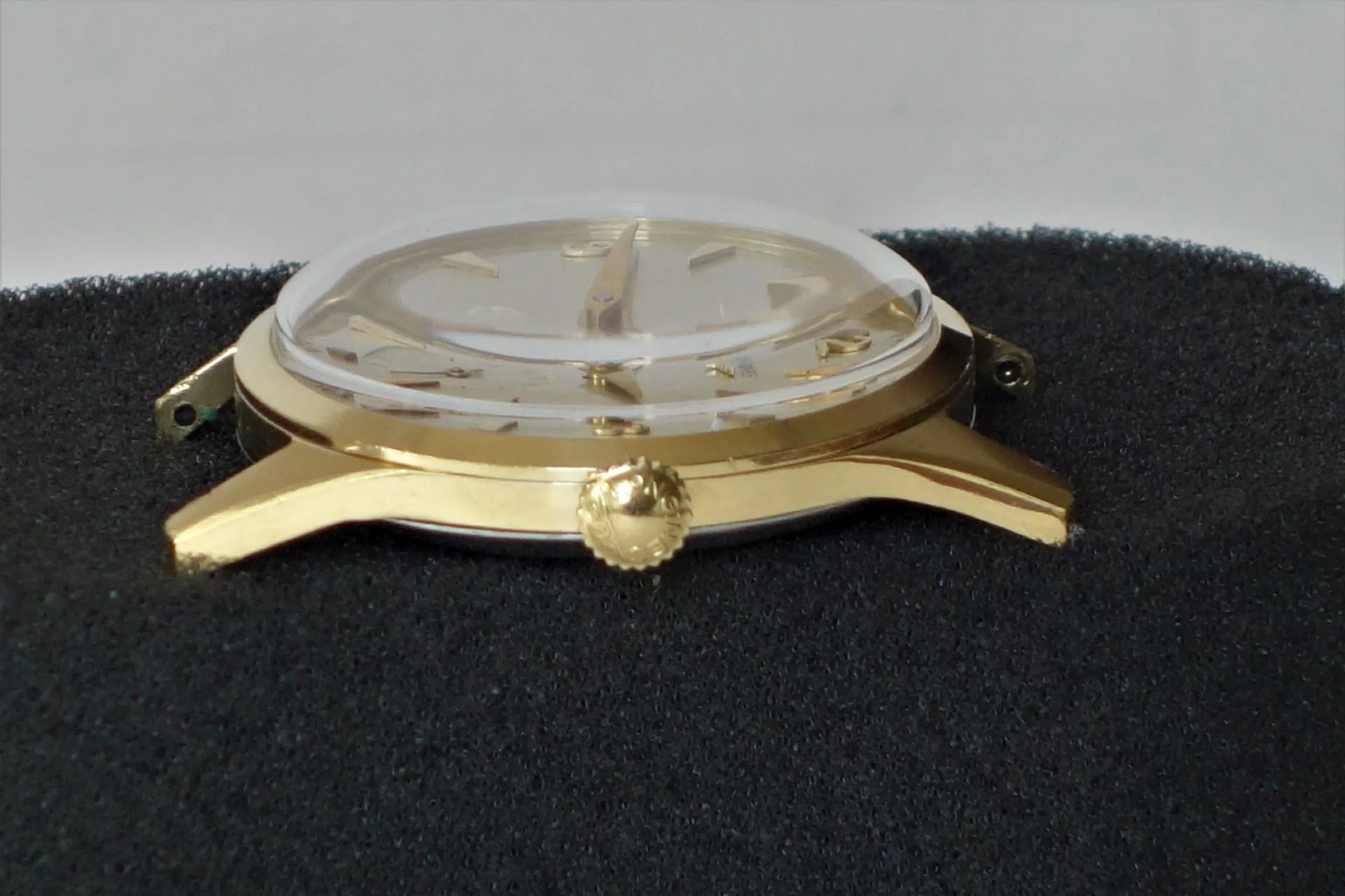 Goldfarbenes Uhrgehäuse mit montiertem Zifferblatt, Zeigern und Glas.