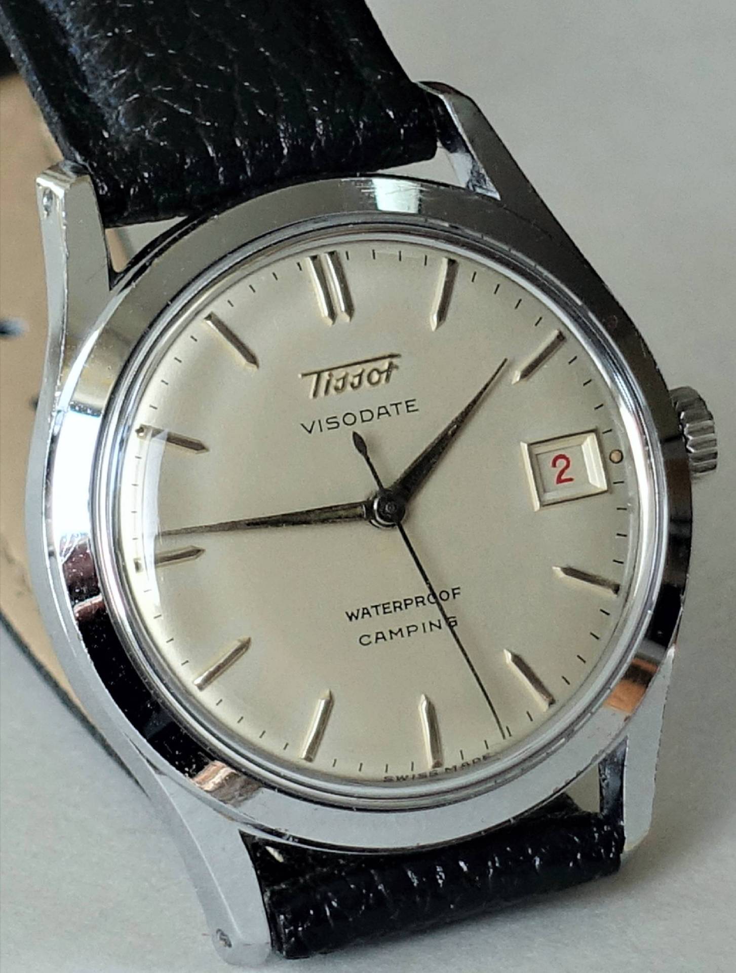 Silberfarbene Armbanduhr mit hellem Zifferblatt, schwarzem Lederarmband und Datumsanzeige.