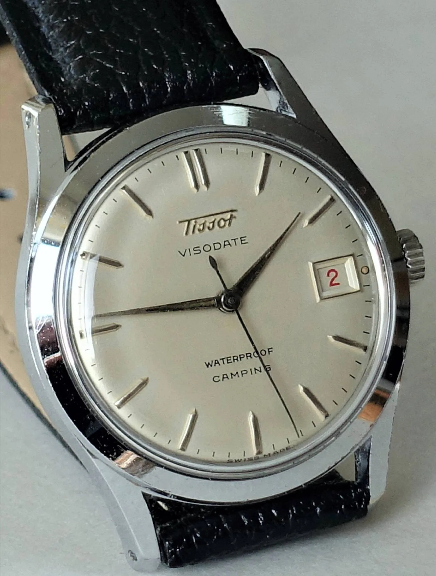 Silberfarbene Armbanduhr mit hellem Zifferblatt, schwarzem Lederarmband und Datumsanzeige.