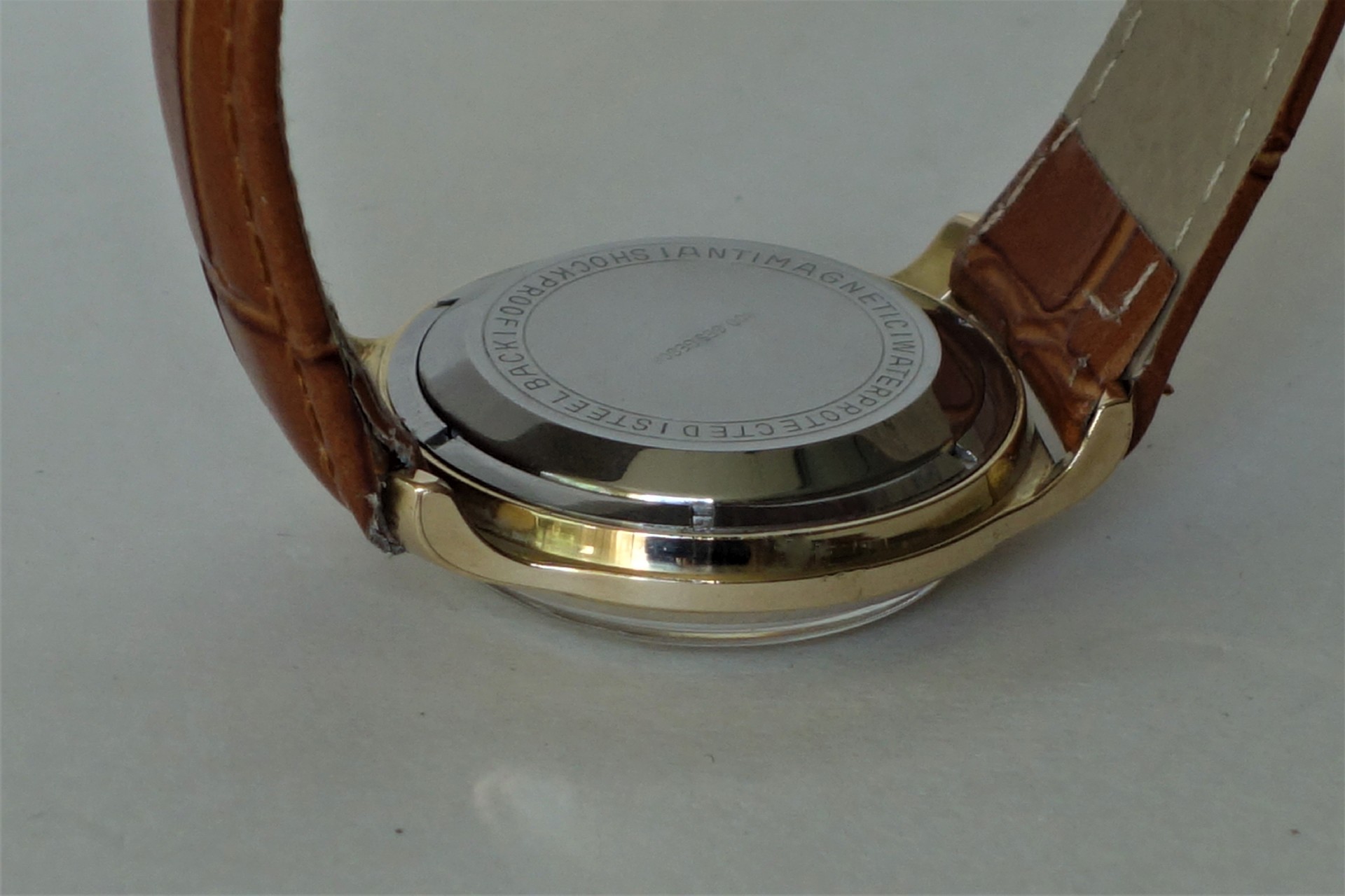 Silberfarbener Uhrenboden mit umlaufender Gravur an einer Uhr mit braunem Armband.