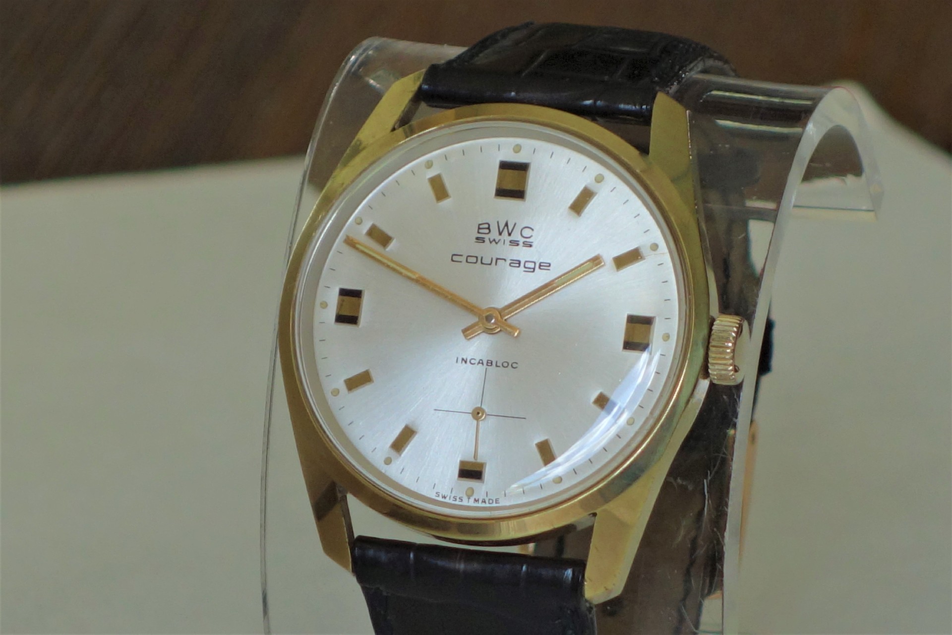 Analoge Armbanduhr mit goldfarbenem Gehäuse, silbernem Zifferblatt und schwarzem Lederarmband.