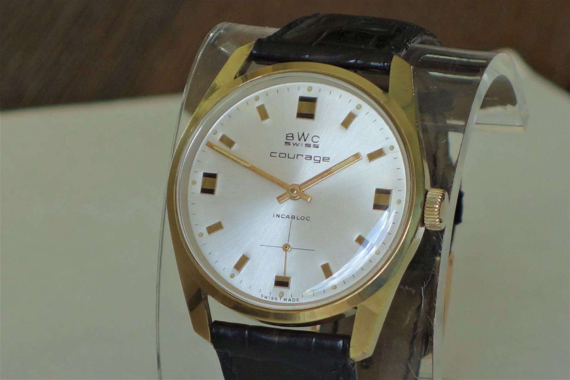 Analoge Armbanduhr mit goldfarbenem Gehäuse, silbernem Zifferblatt und schwarzem Lederarmband.