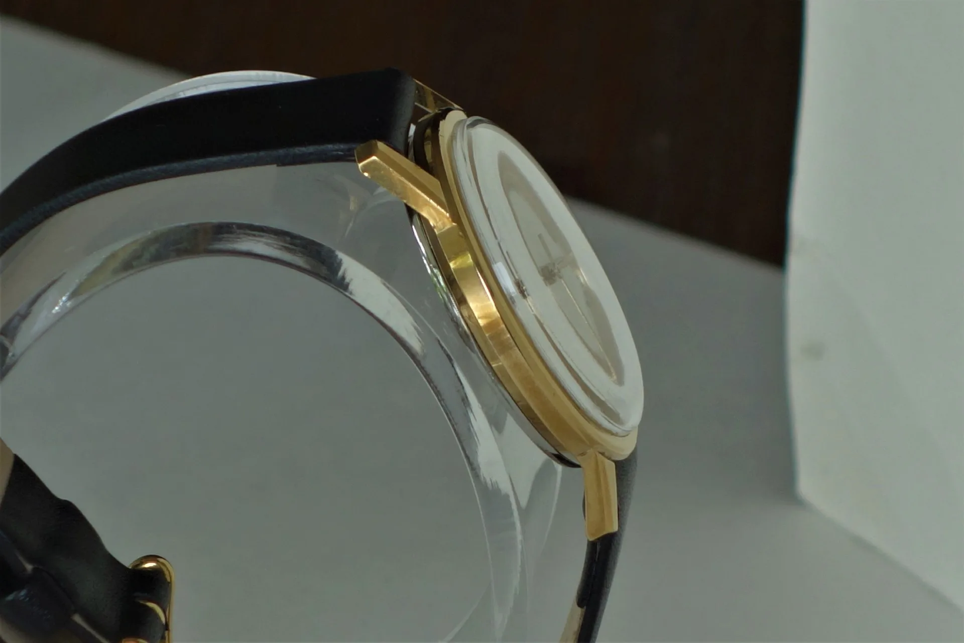 Flache Armbanduhr mit goldfarbenem Gehäuse und schwarzem Armband in seitlicher Ansicht.
