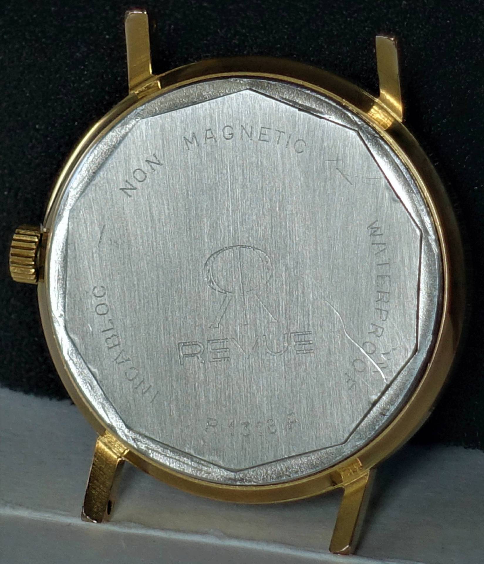 Rundes Uhrgehäuse in goldfarbener Ausführung mit silberfarbener Rückseite und Revue-Gravur.