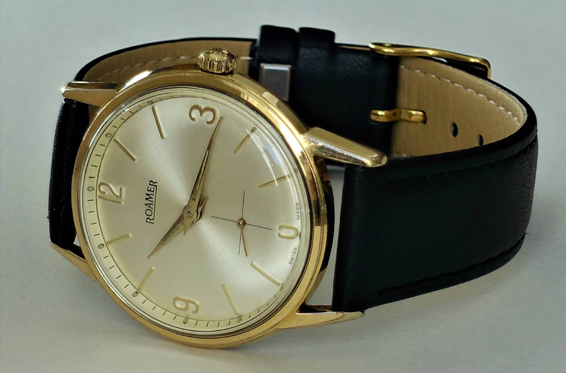 Goldfarbene Armbanduhr mit hellem Zifferblatt und schwarzem Armband.