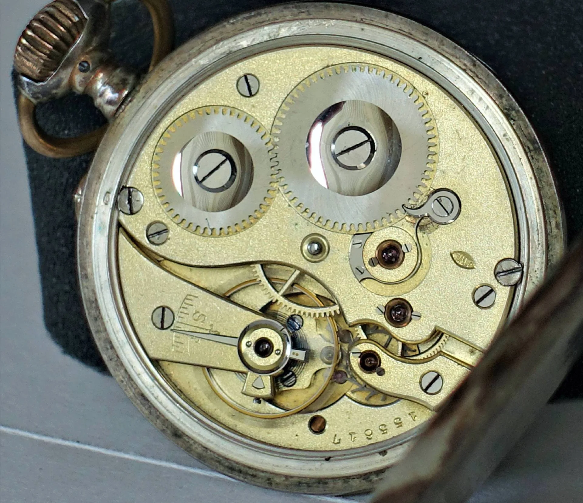 Mechanisches Uhrwerk einer Taschenuhr in silberner Farbe mit sichtbaren Zahnrädern und Schrauben.