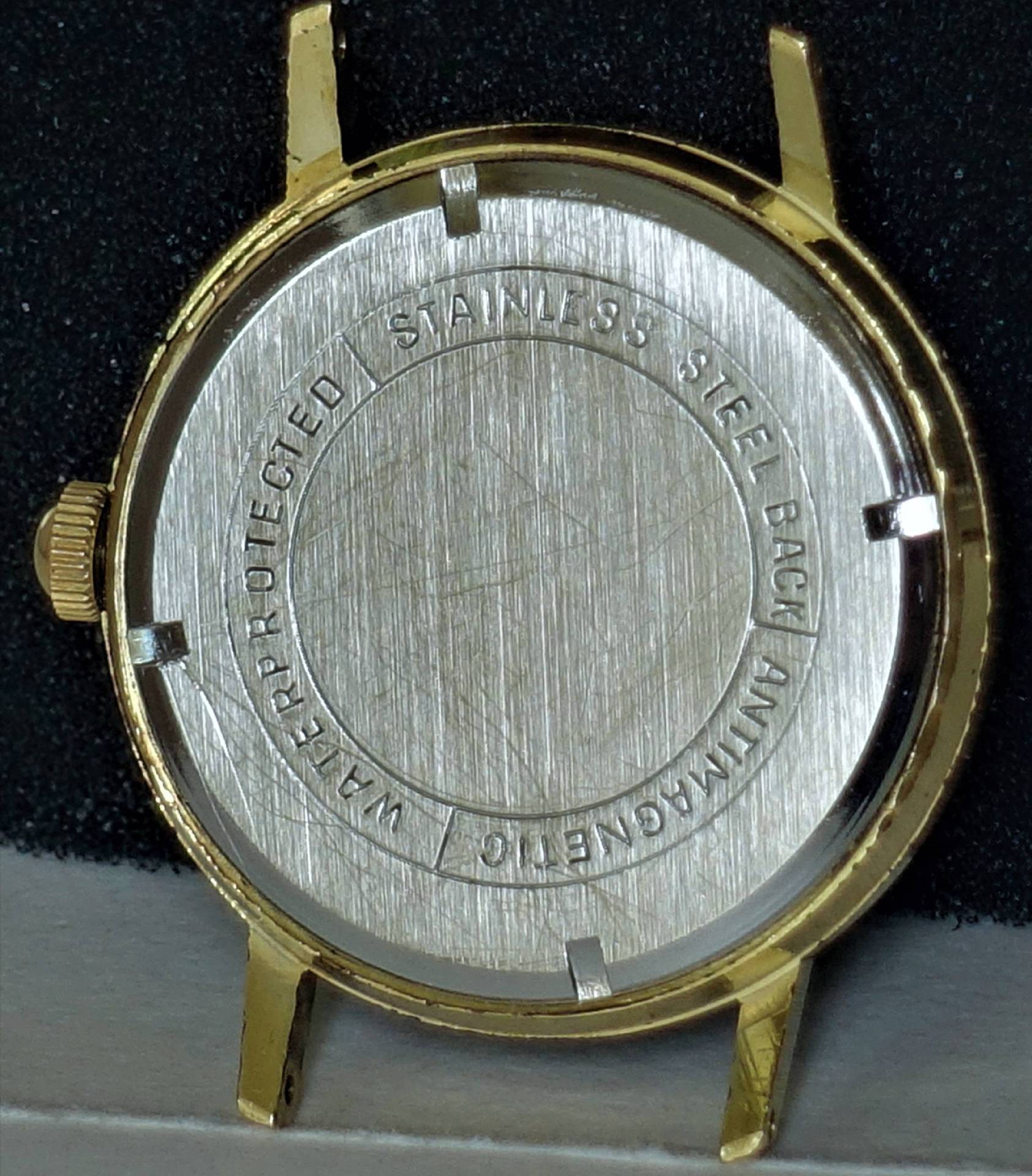 Rundes Uhrengehäuse in goldfarbener Ausführung mit silberfarbener Rückseite aus Metall.