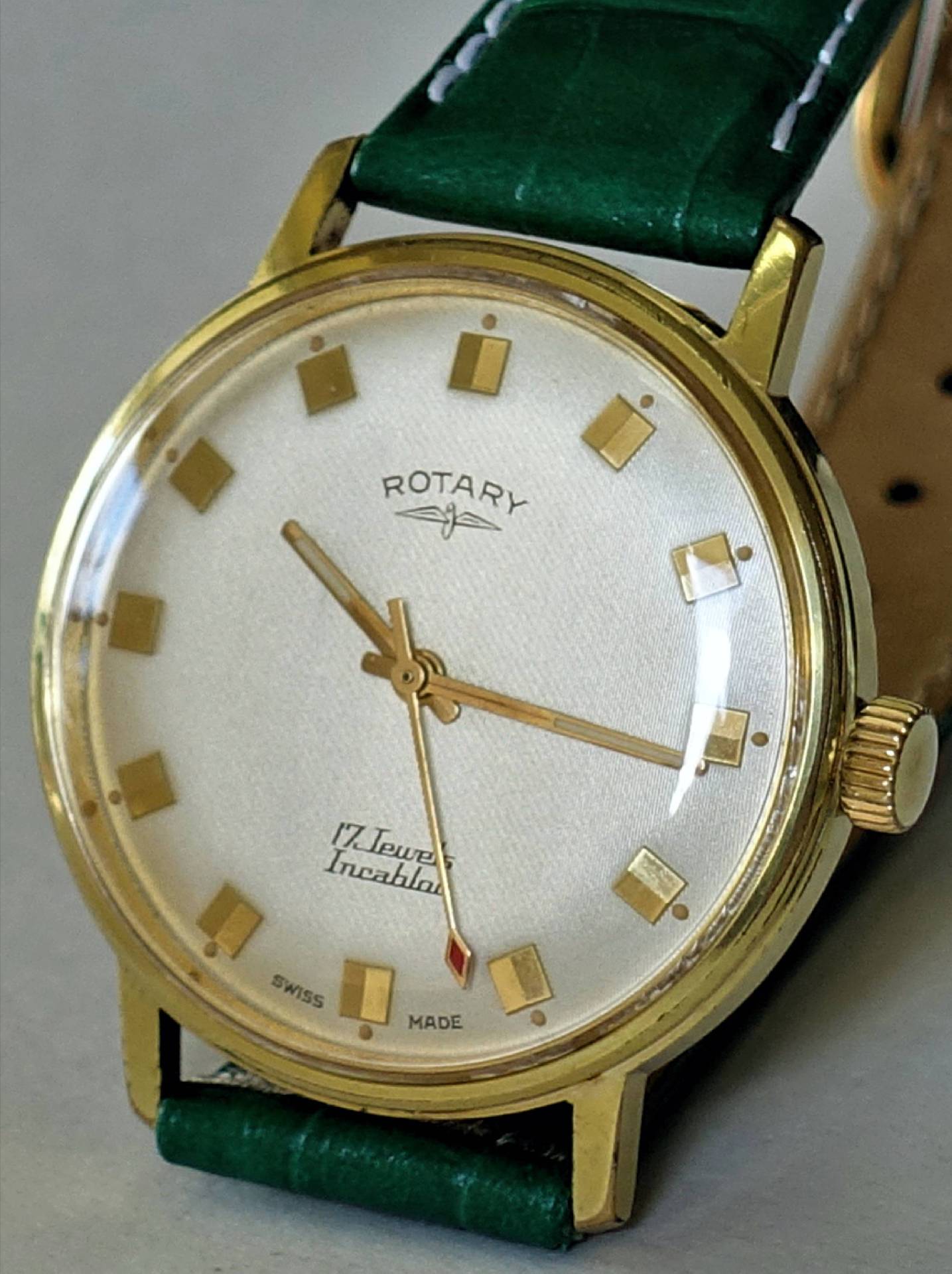 Goldfarbene Armbanduhr mit weißem Zifferblatt und grünem Armband.