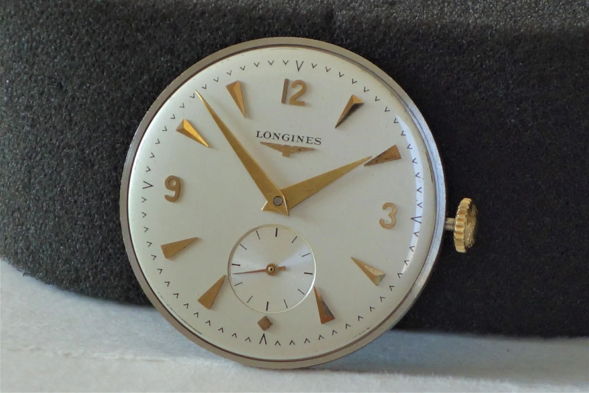Uhrwerk mit Zifferblatt Longines Rundes Uhrwerk mit weißem Zifferblatt und goldfarbenen Zeigern sowie goldfarbener Krone, Marke Longines.