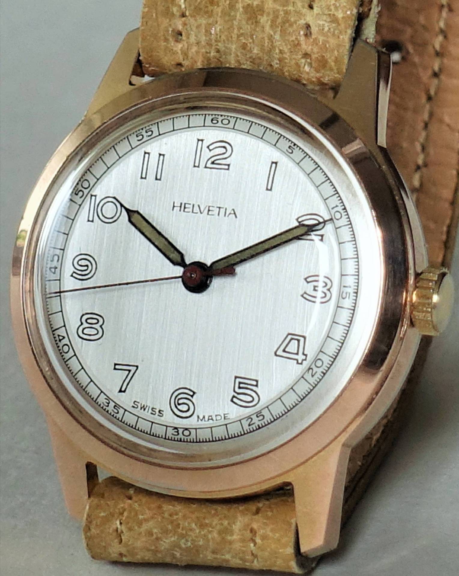 Beige Armbanduhr mit silberfarbenem Zifferblatt und braunem Lederarmband.