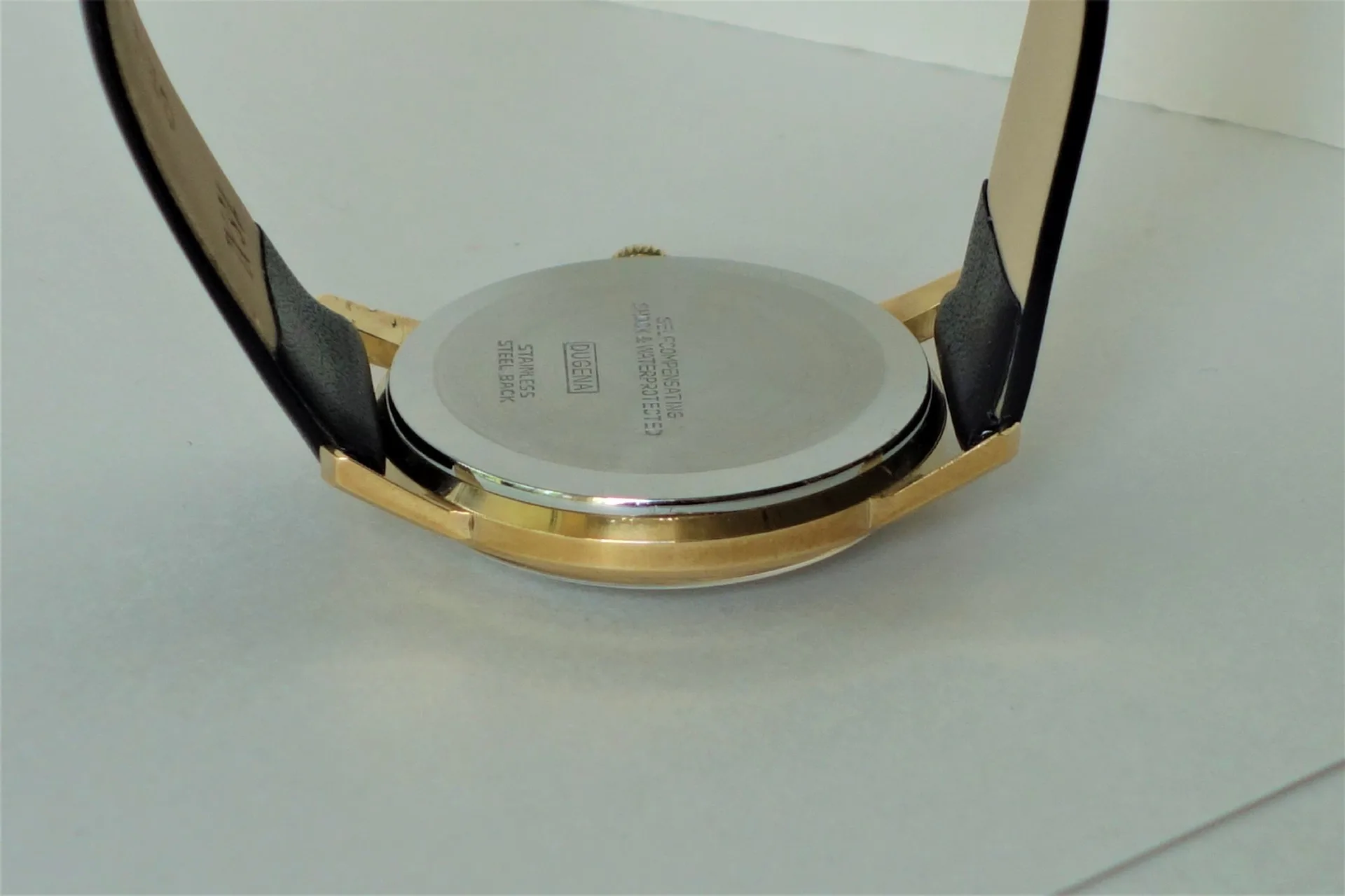 Silberfarbener Uhrenboden mit schwarzem Armband und goldfarbenem Gehäuserand.