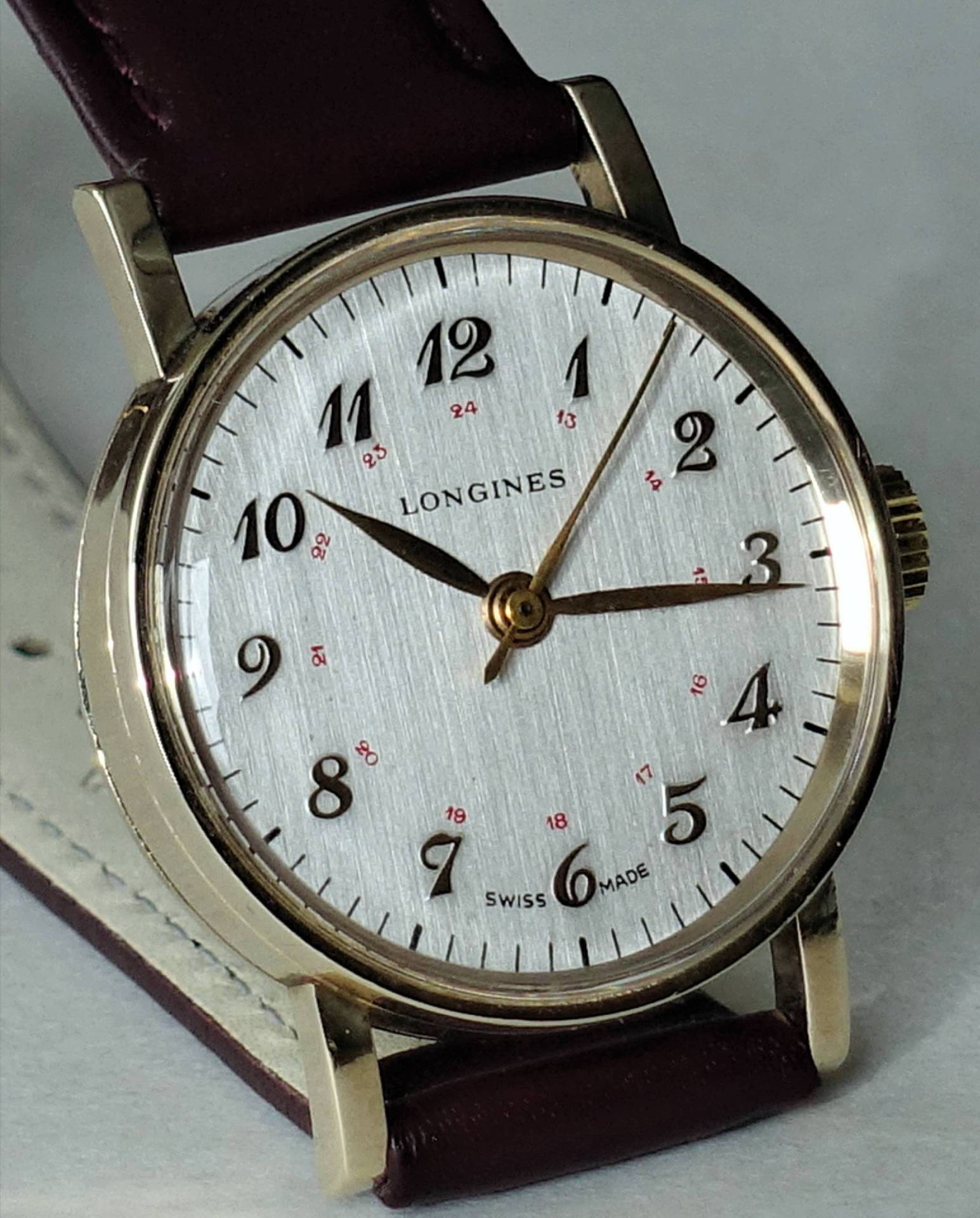 Longines Uhr mit silbernem Ziffernblatt, arabischen Ziffern und braunem Lederarmband