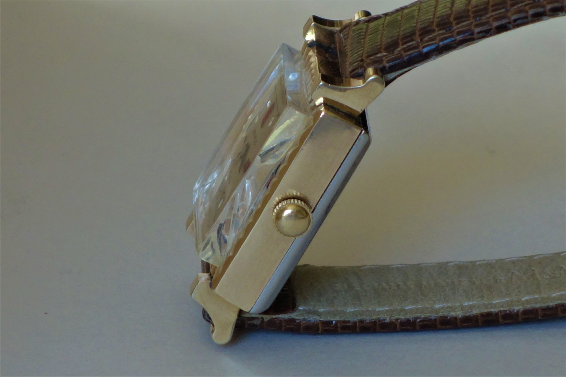 Rechteckige Armbanduhr mit goldfarbenem Gehäuse, braunem Lederarmband und gewölbtem Uhrglas.
