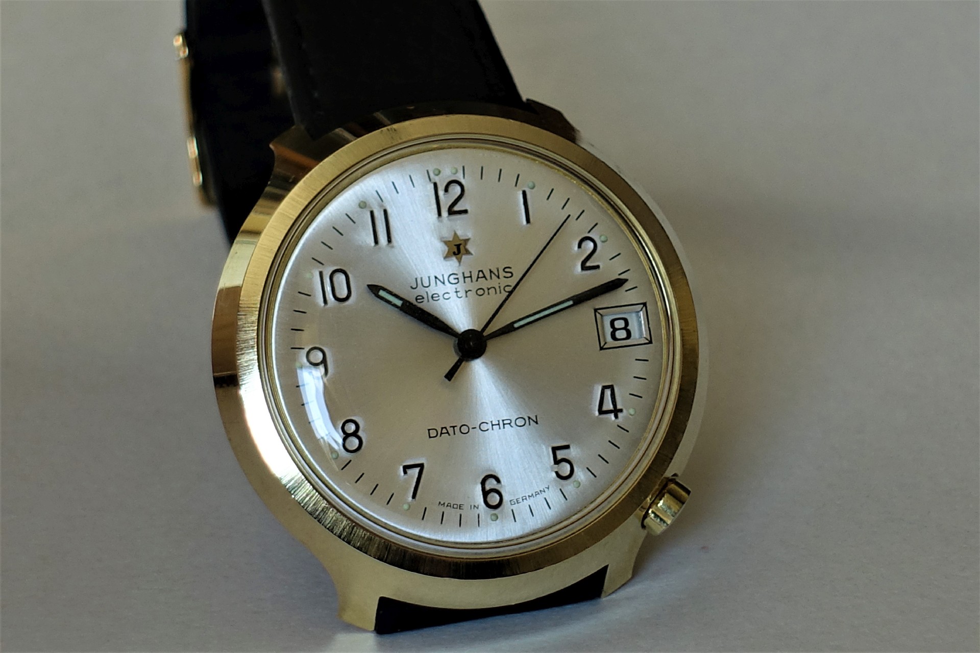 Analoge Armbanduhr mit hellem Zifferblatt, schwarzem Lederarmband und goldfarbenem Gehäuse.