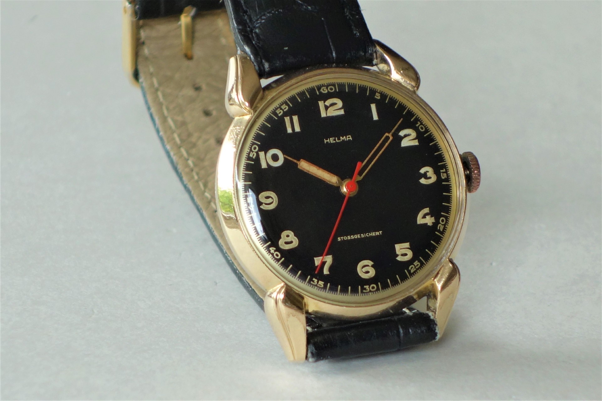 Analoge Armbanduhr mit schwarzem Zifferblatt, goldfarbenem Gehäuse und schwarzem Armband.