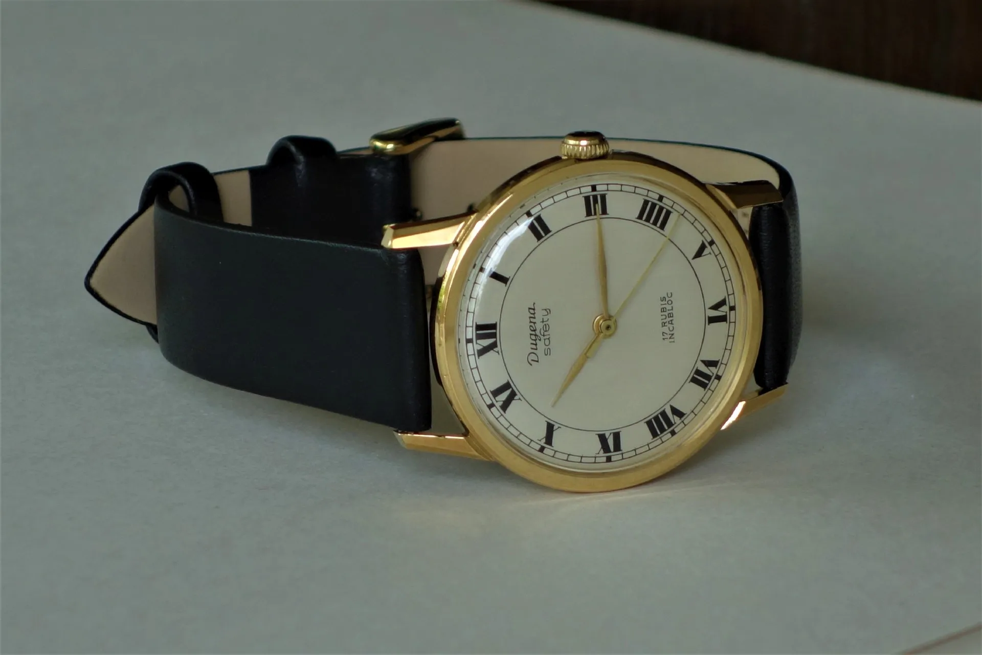 Klassische Armbanduhr mit goldfarbenem Gehäuse, weißem Zifferblatt und schwarzem Lederarmband.
