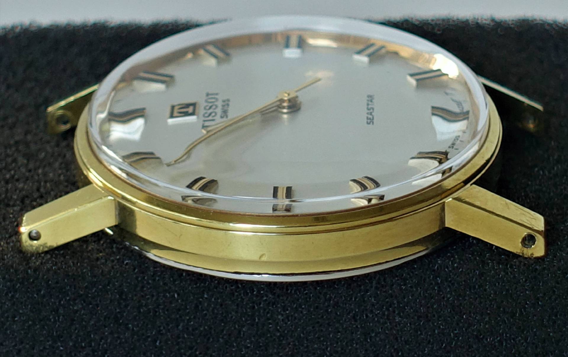 Flache Armbanduhr mit goldfarbenem Gehäuse und hellem Zifferblatt ohne Armband.