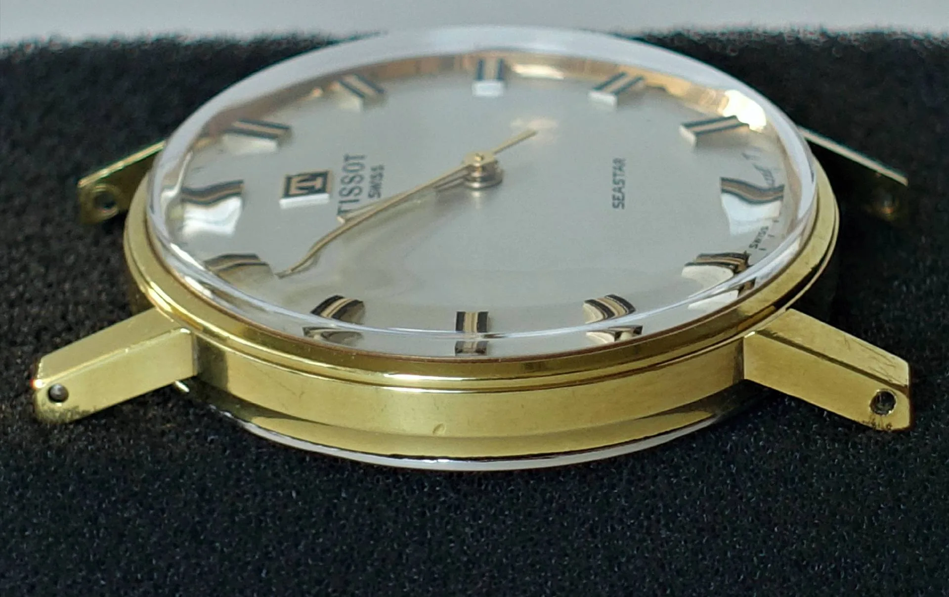 Flache Armbanduhr mit goldfarbenem Gehäuse und hellem Zifferblatt ohne Armband.
